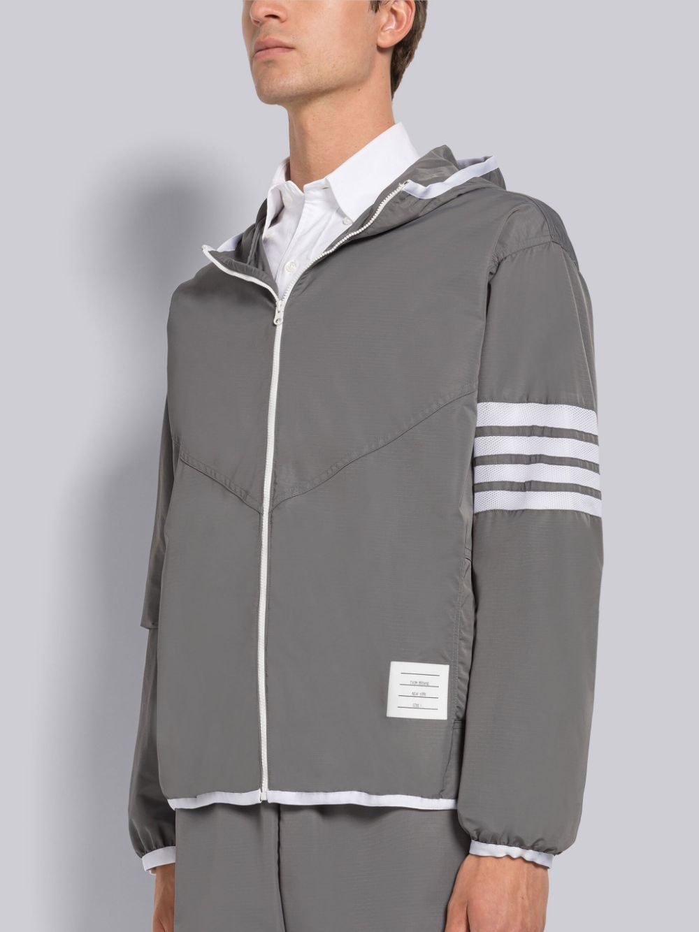 Thom Browne track jacket in grey, with four white bands on the left arm.