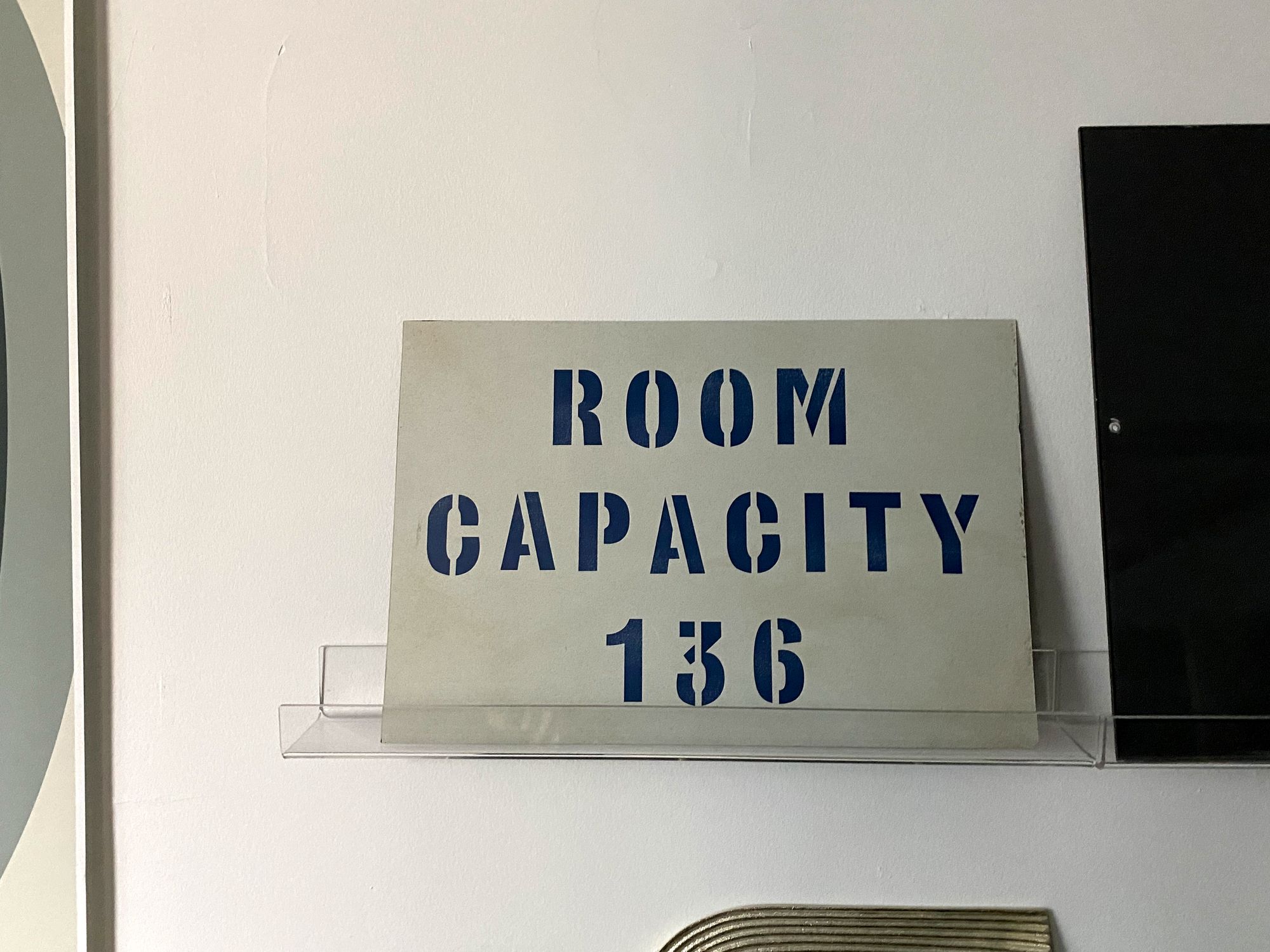 Stencilled sign: ROOM CAPACITY 136