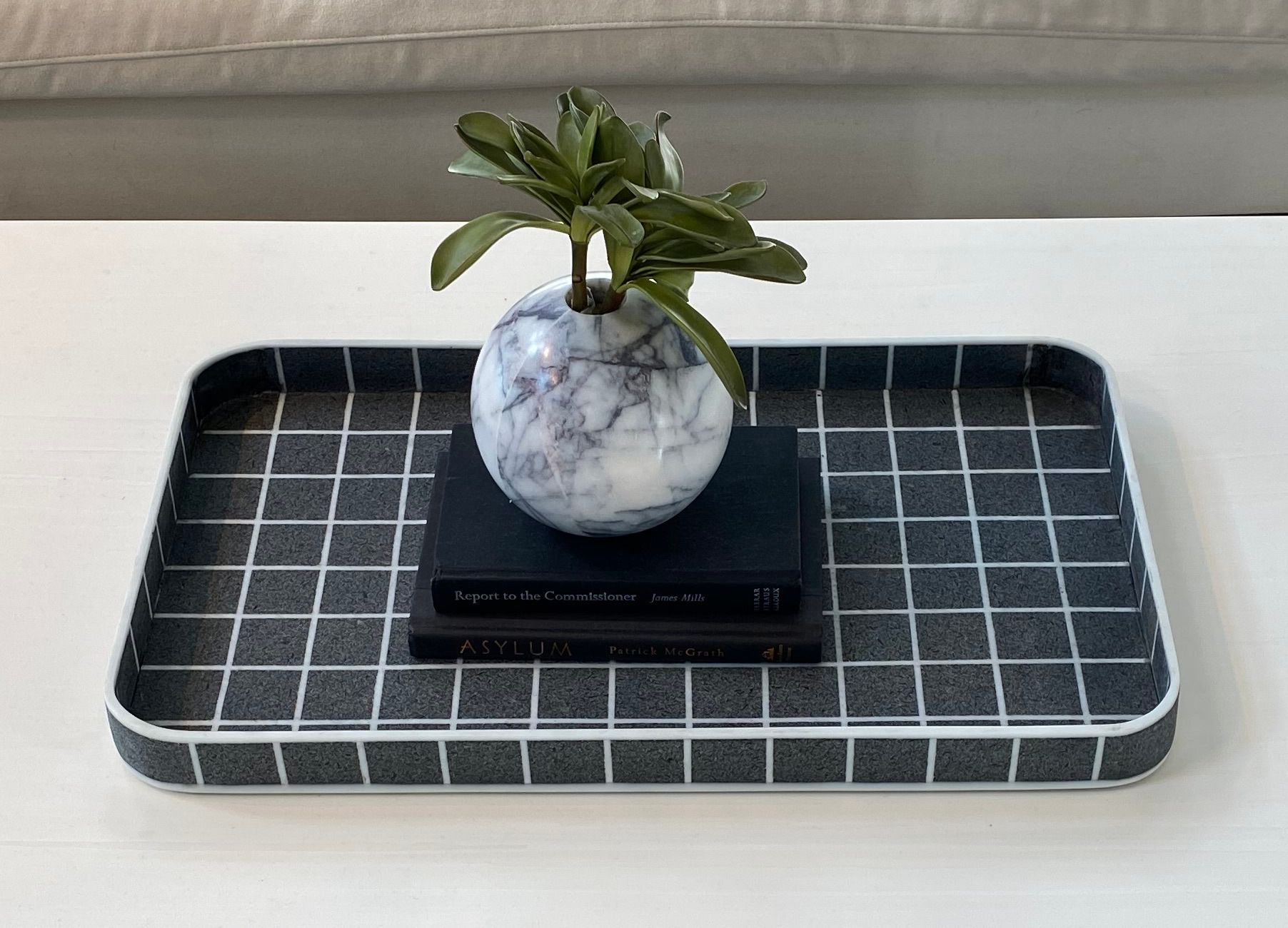 A tray holding two books which support a vase with some greenery