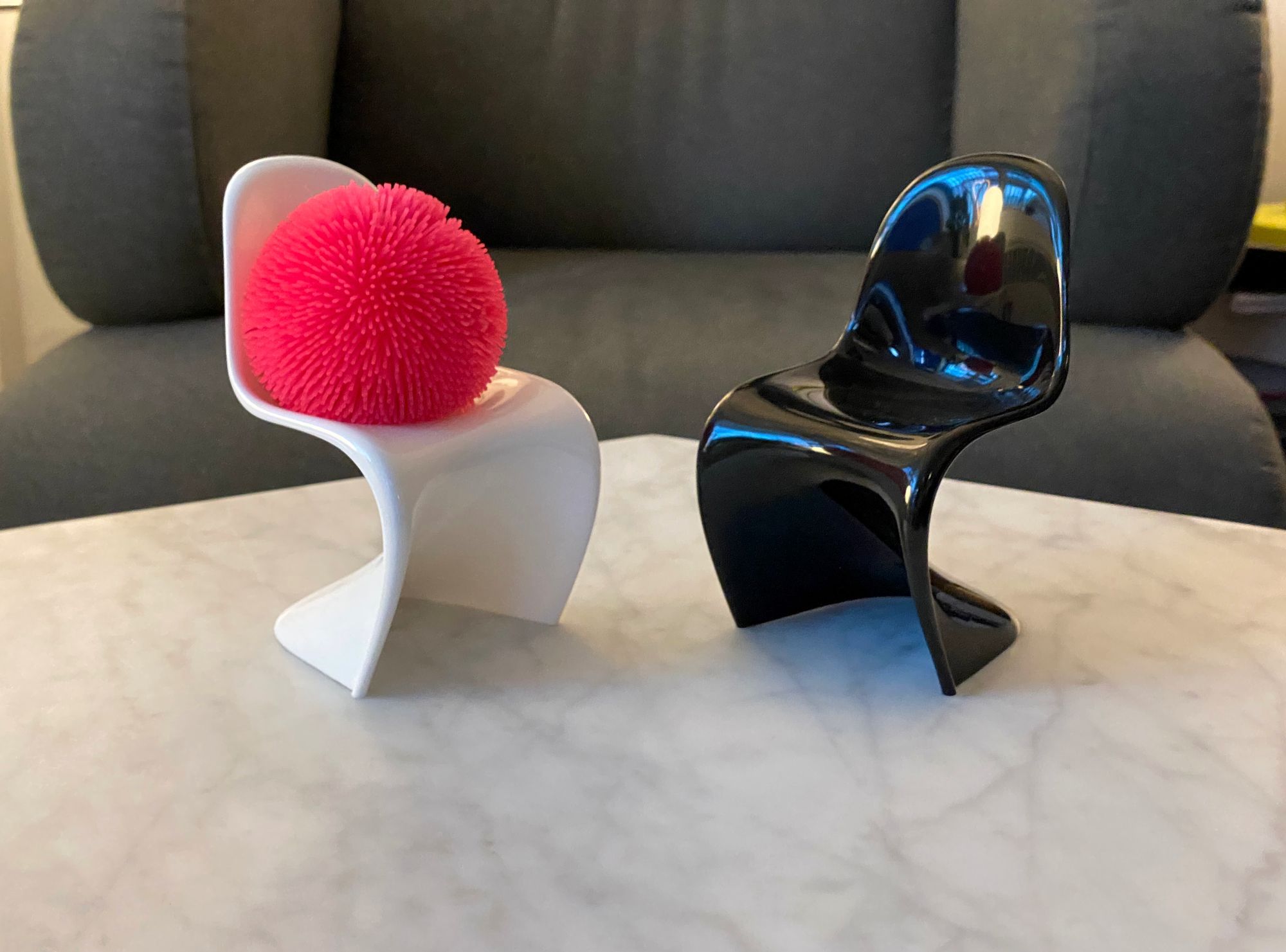 Two miniature Panton chairs on a coffee table, one holding a bright pink stress-relief toy.