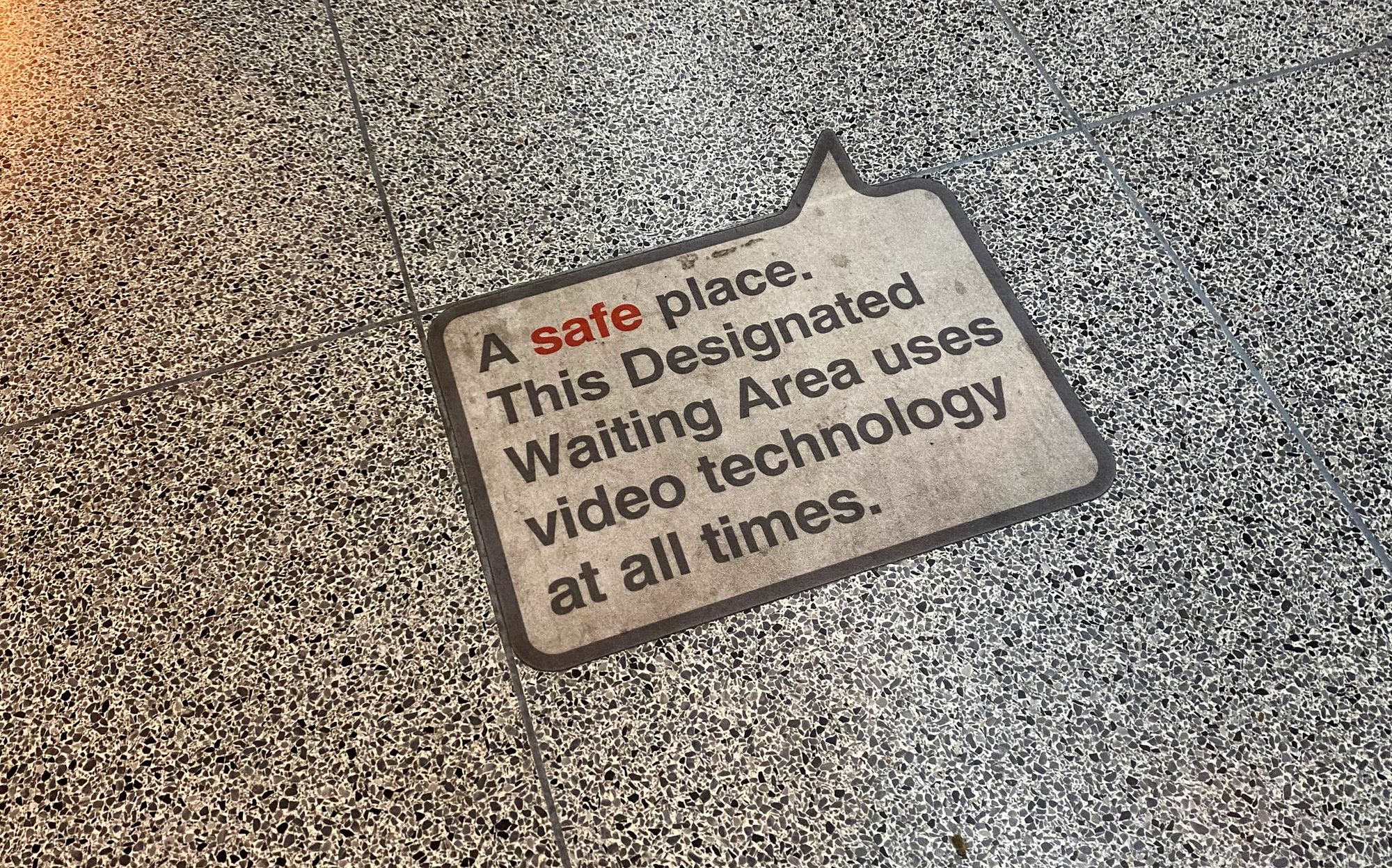 A floor sticker that reads: A safe place. This Designated Waiting Area uses video technology at all times.