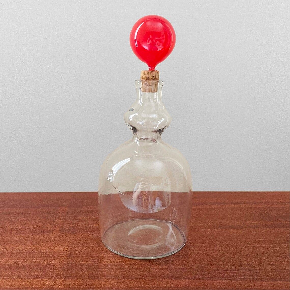 Transparent decanter with a bright red stopper.