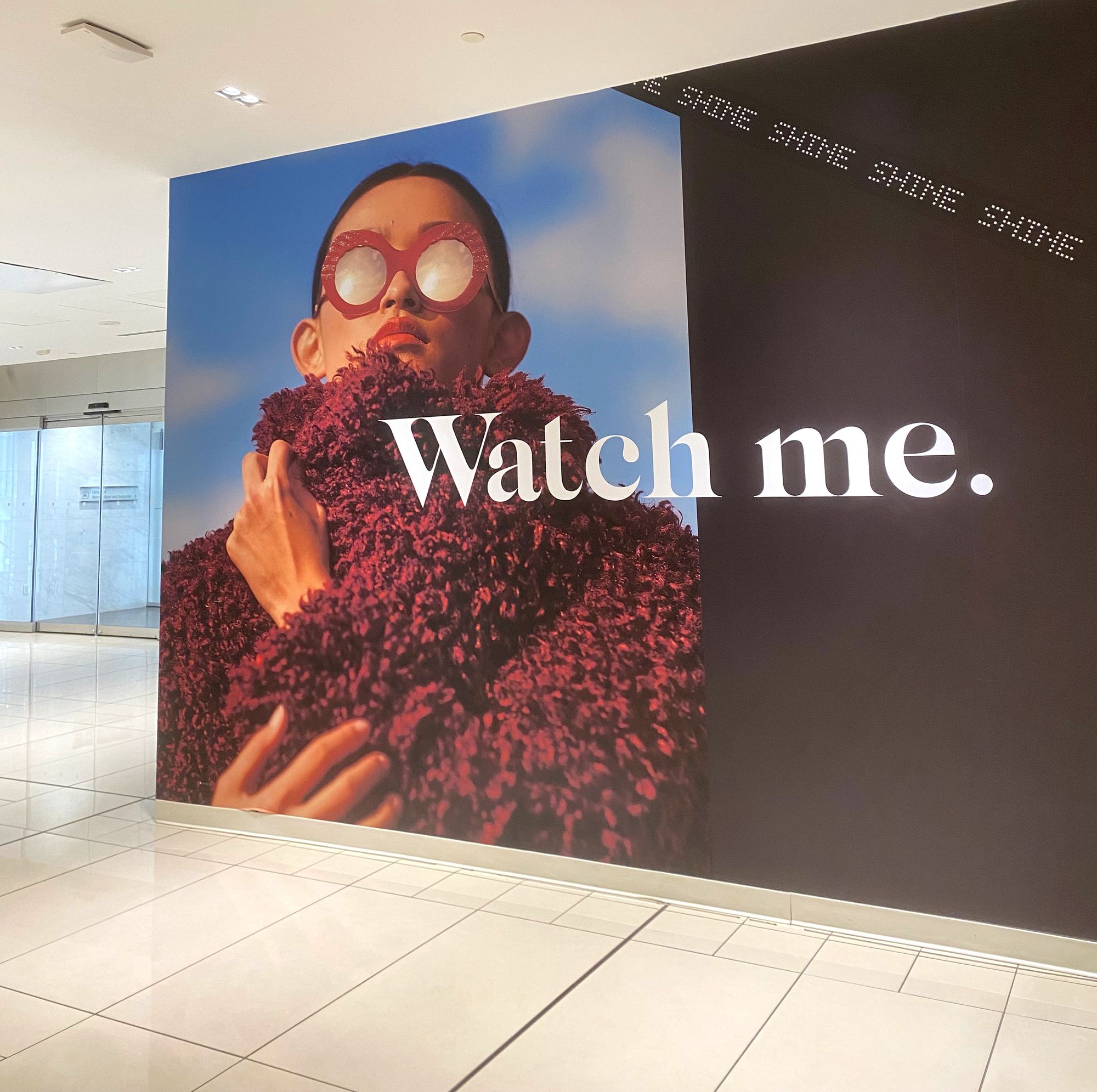 Gigantic wall-mounted ad at The Manulife Centre promoting the venue as a place for influencers. The slogan is "Watch me" and the image is of a trendy young woman.