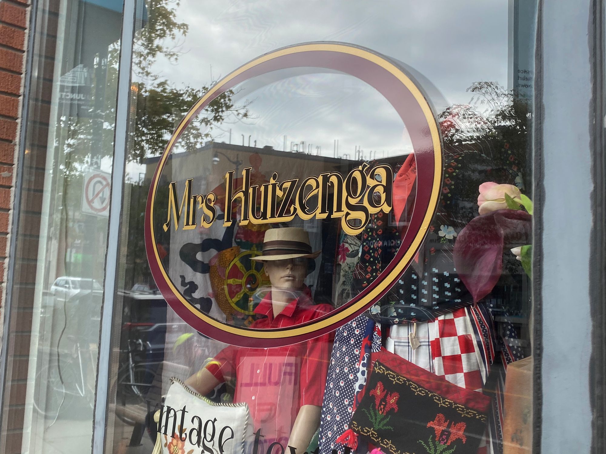 Window of Mrs. Huizenga showing a mannequin in a red shirt and fedora, plus a jumble of other items.