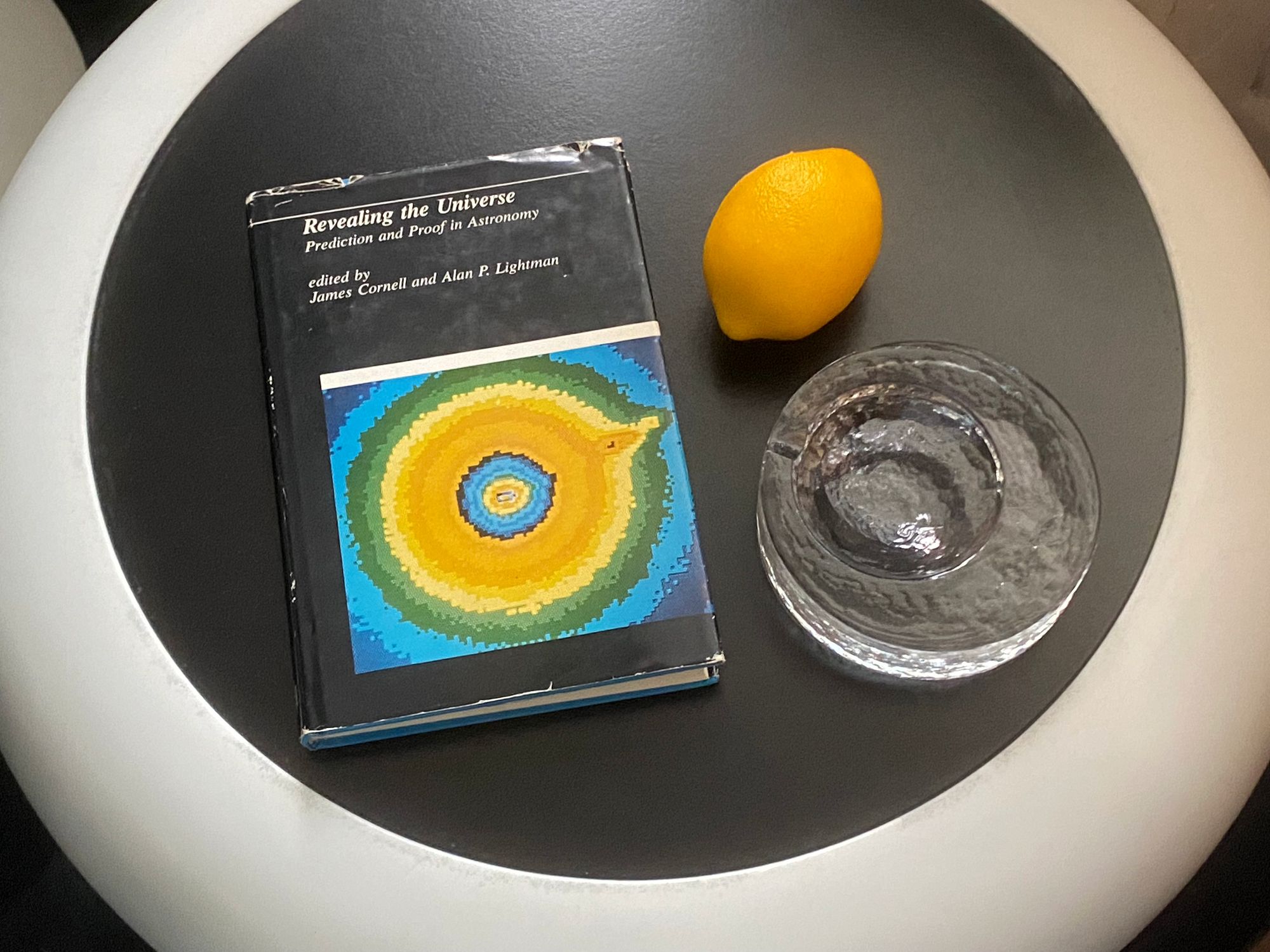 "Revealing the Universe" on a side table with a fake lemon and an ashtray.