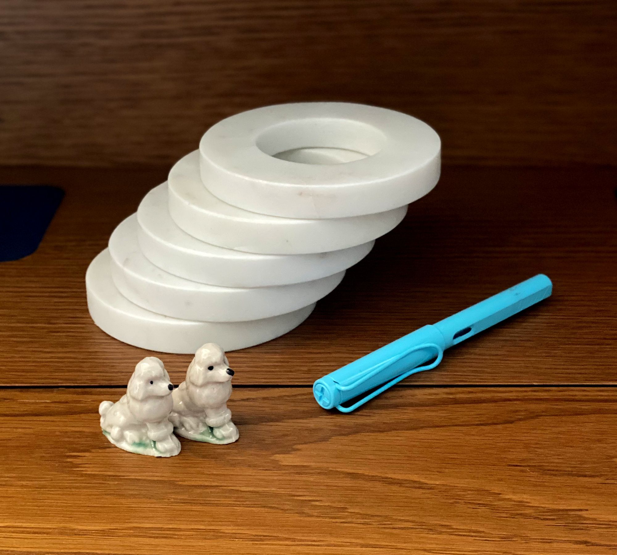 Stacked paperweights, pair of poodle figurines,and LAMY pen on a desktop.