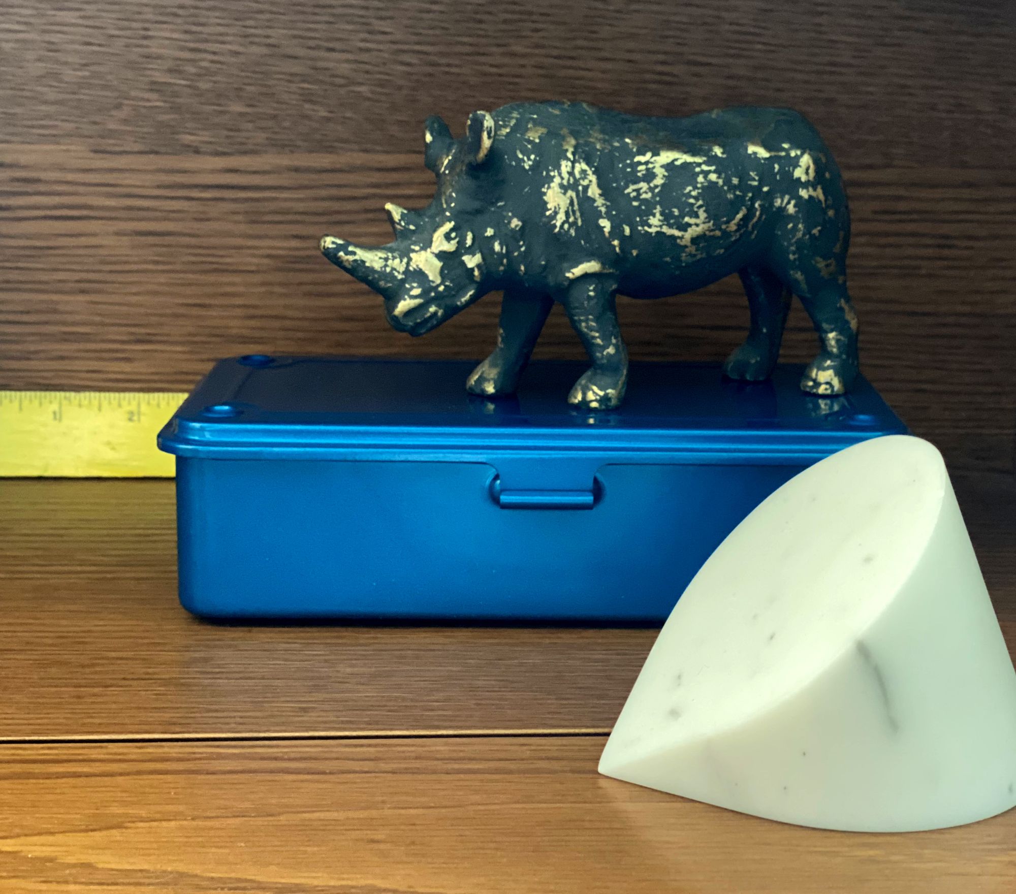 Ruler, metal box, rhinoceros figurine and marble paperweight on a desktop.