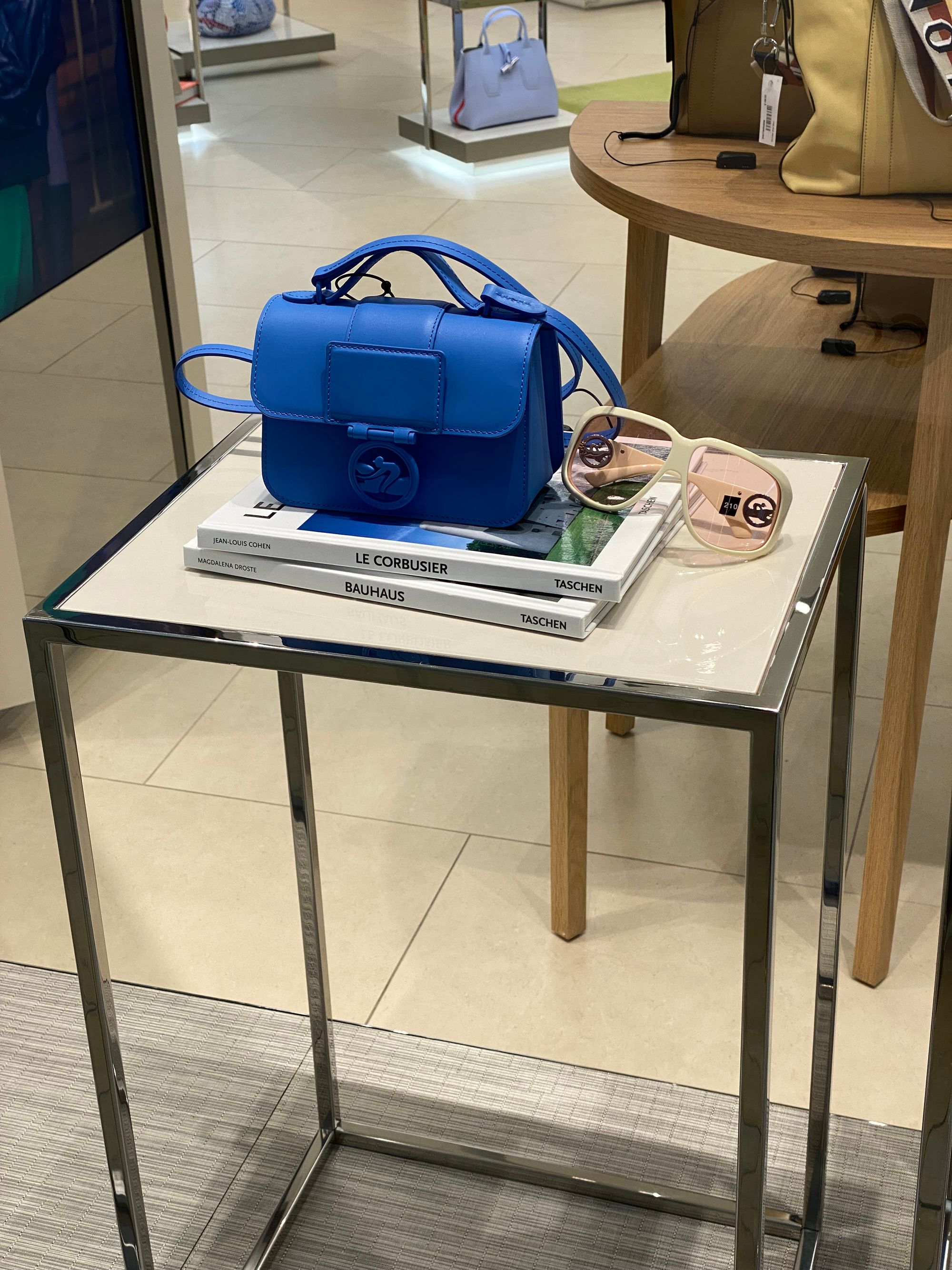 Blue Longchamps purse and pair of sunglasses resting on two art books.