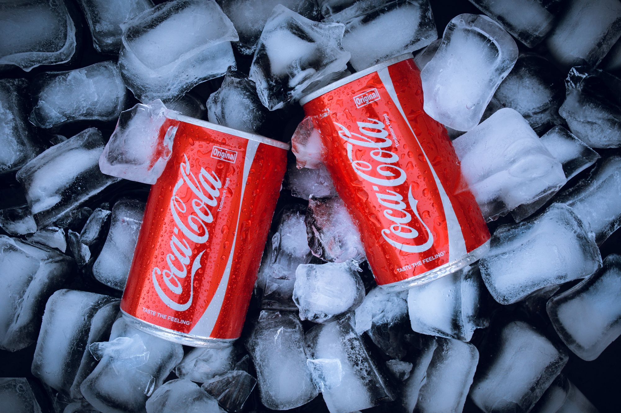 Two cans of Coca-Cola resting in a lot of ice cubes.