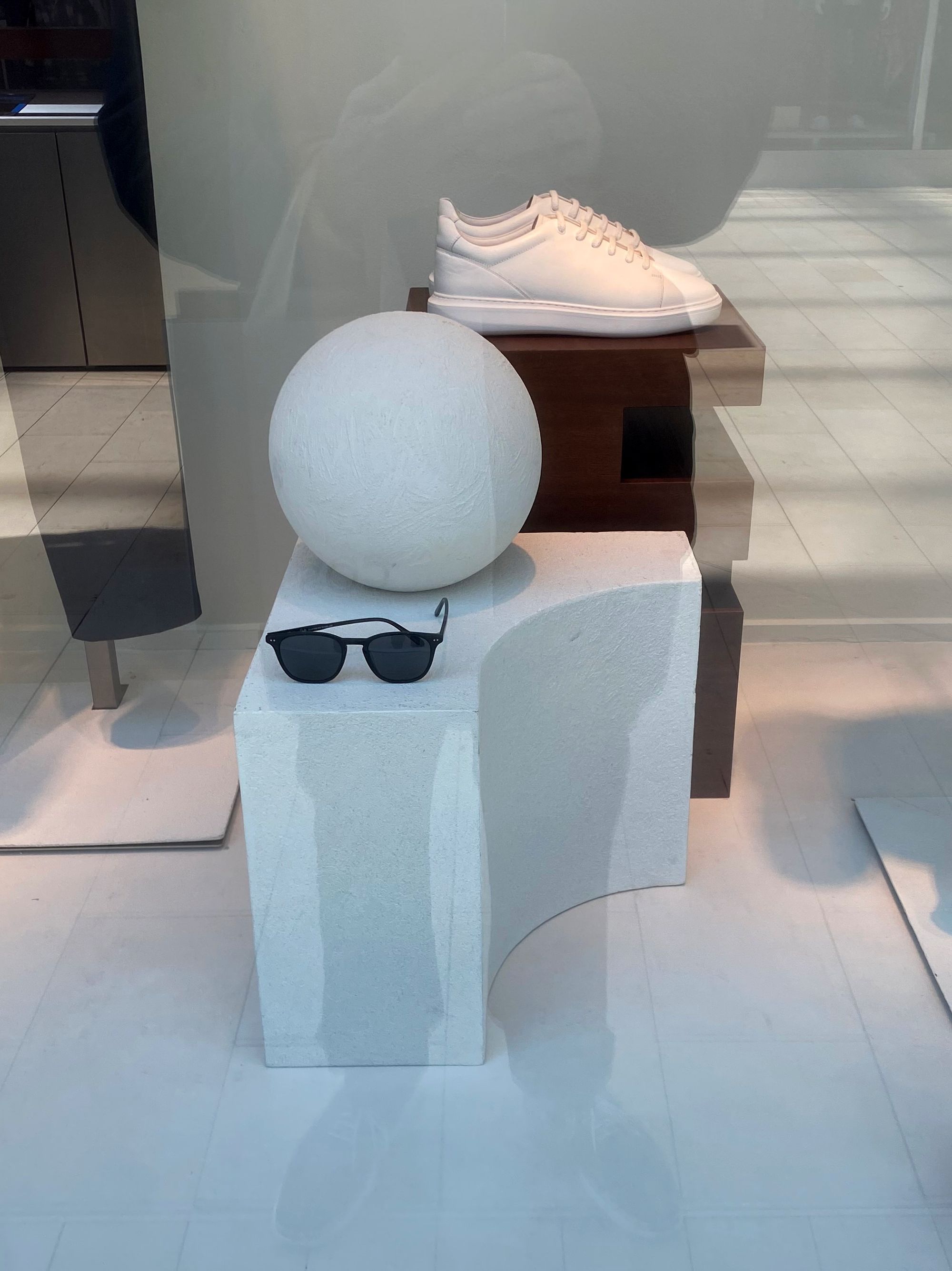 Shop window display with sphere, pair of sunglasses, and pair of white sneakers.