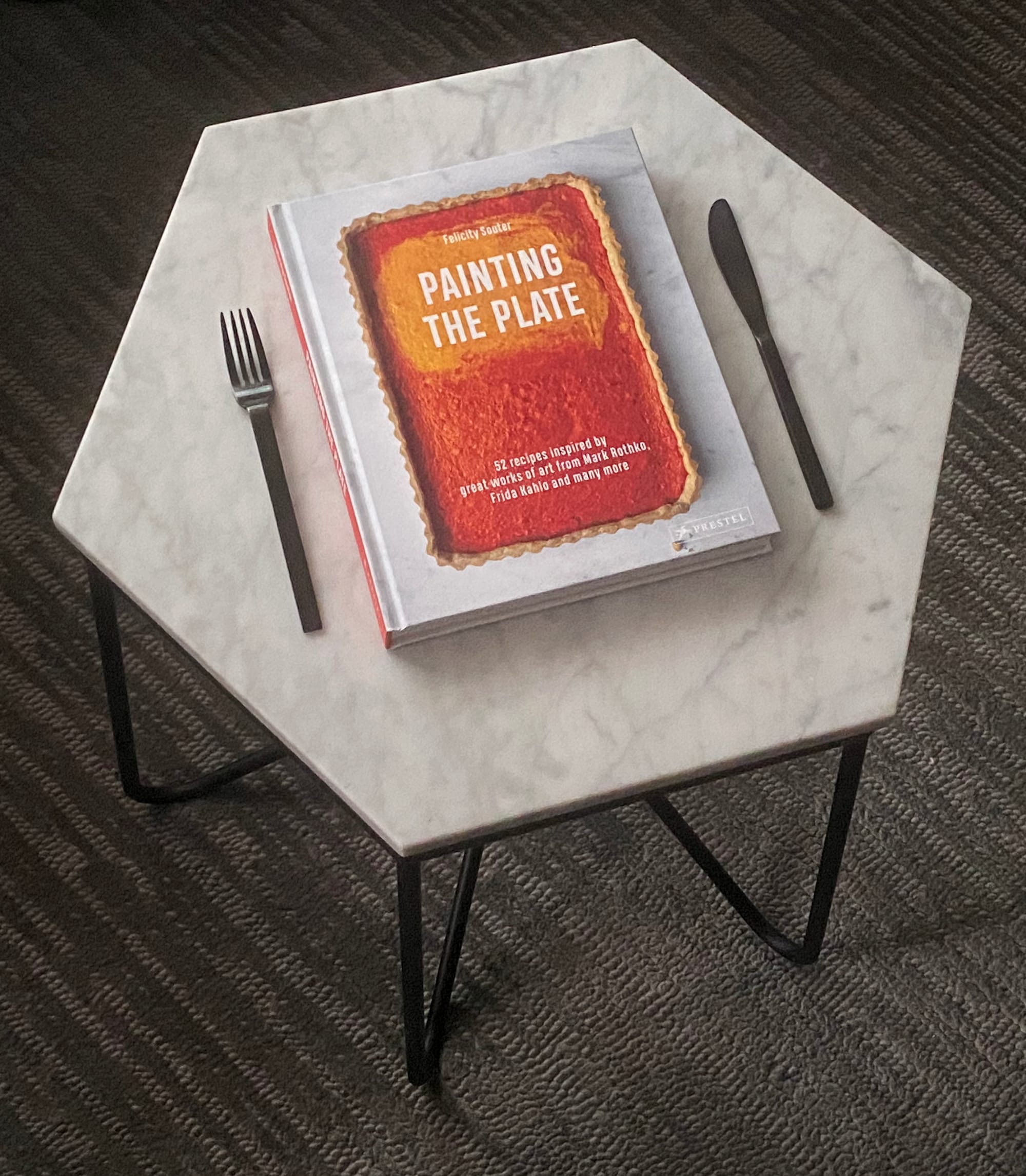 "Painting the Plate" on a coffee table, bracketed by a fork and knife.