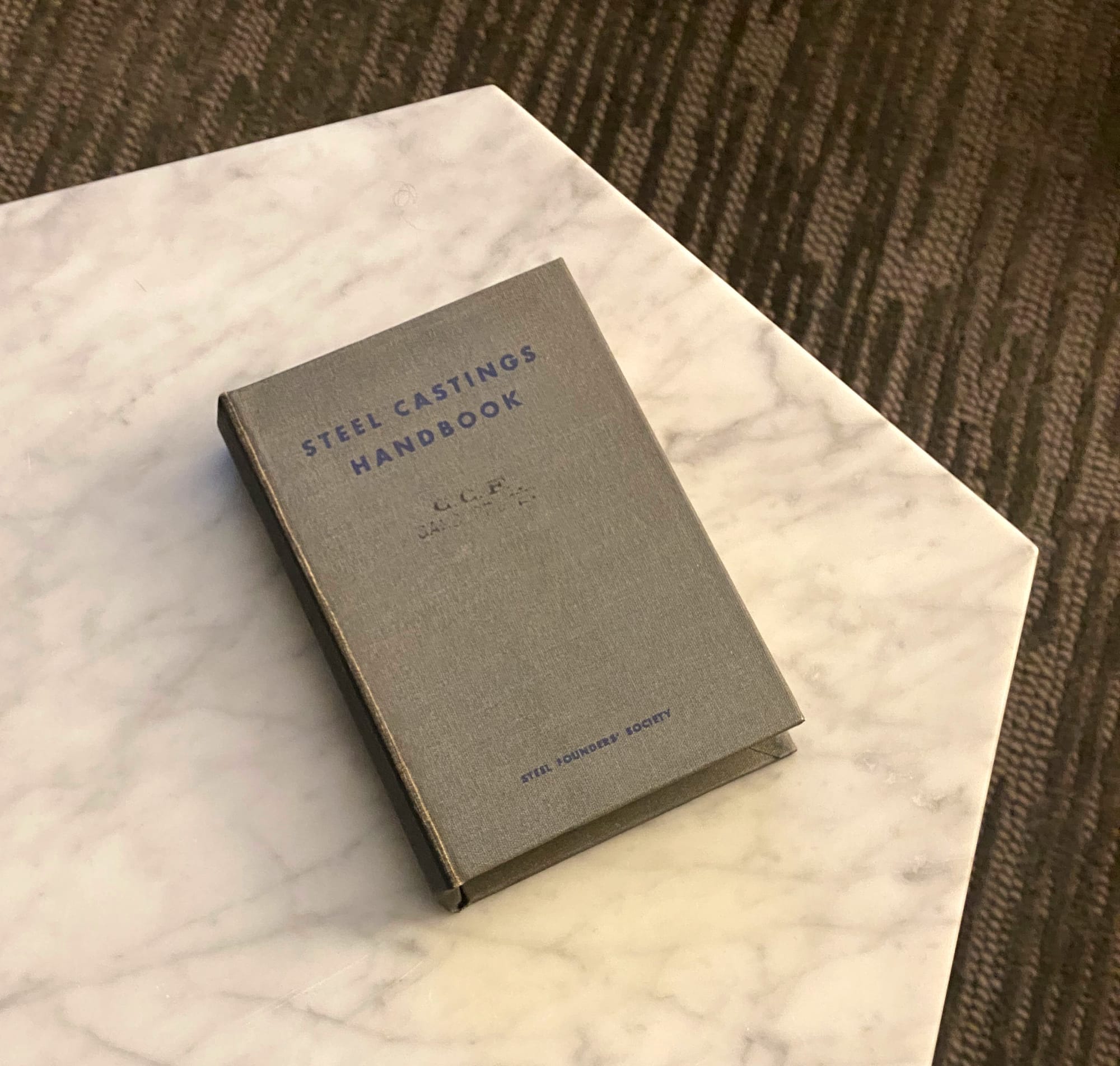 Book titled "Steel Castings Handbook" on a white marble tabletop.