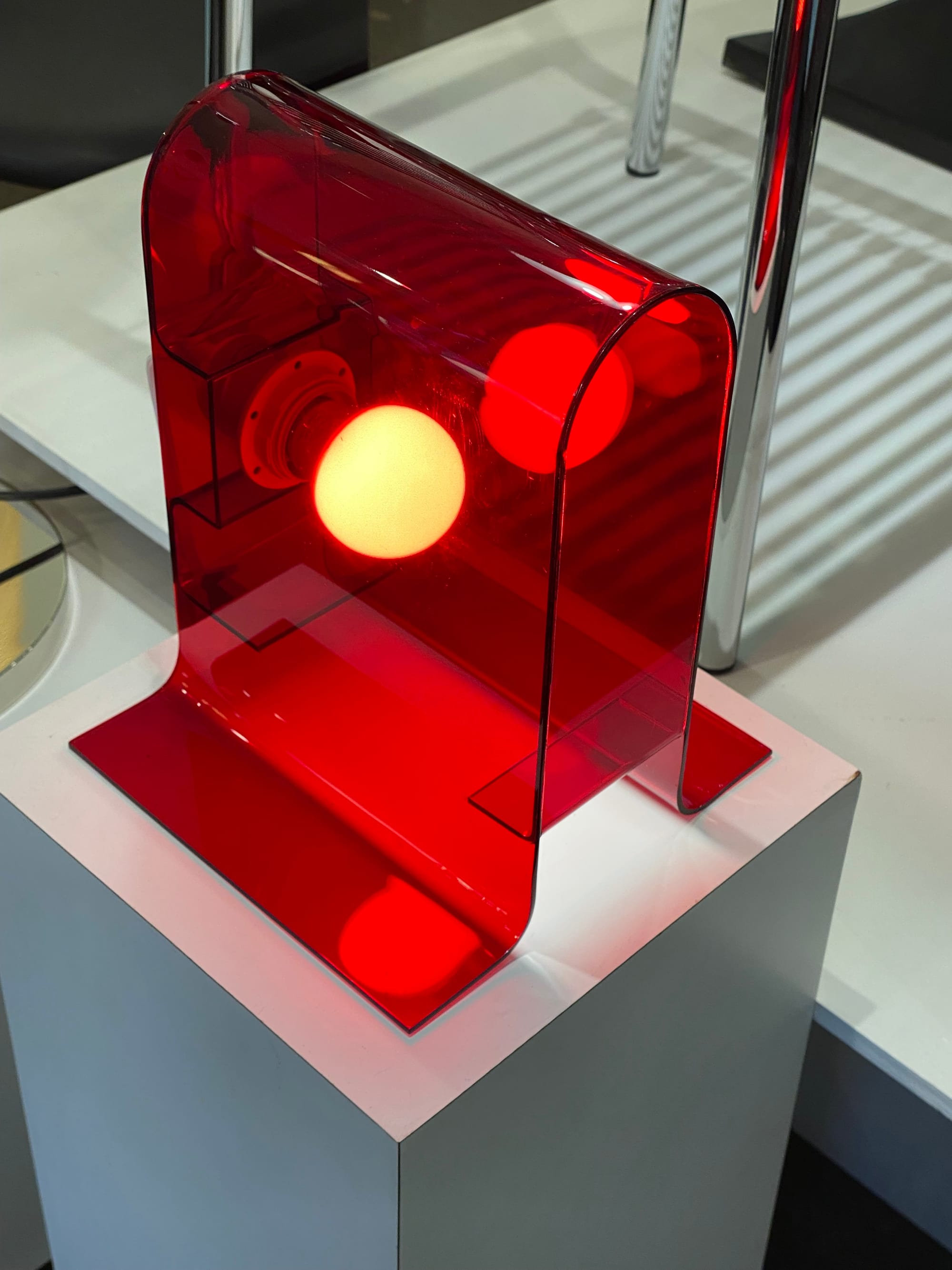 Table lamp made of transparent red acrylic with a lightbulb switched on inside.