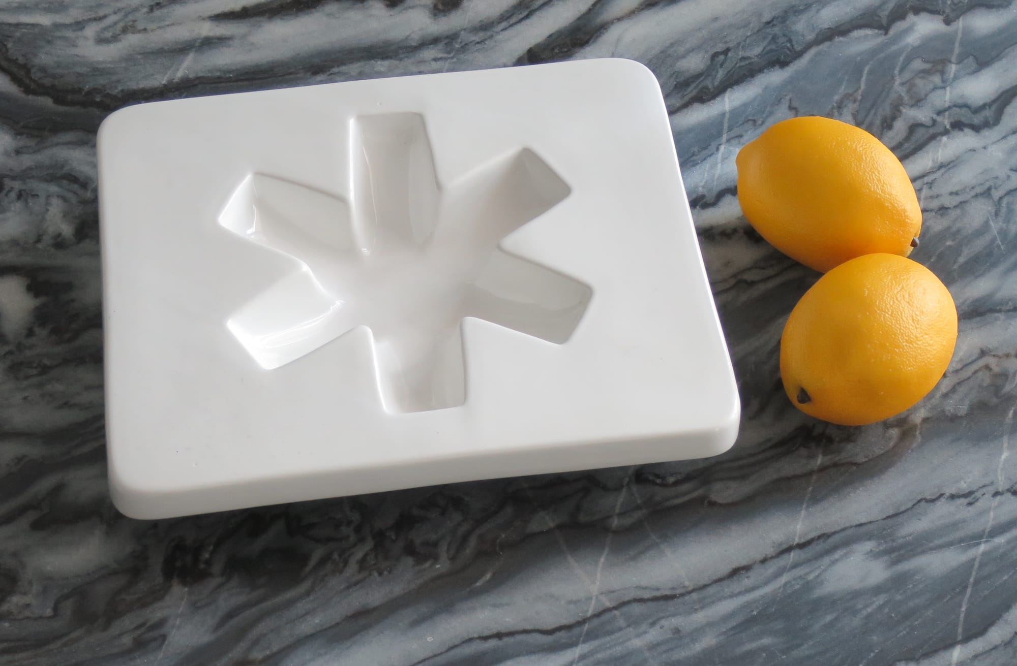 Glossy white ashtray with a flat surface and asterisk-shaped indentation, beside two fake lemons.