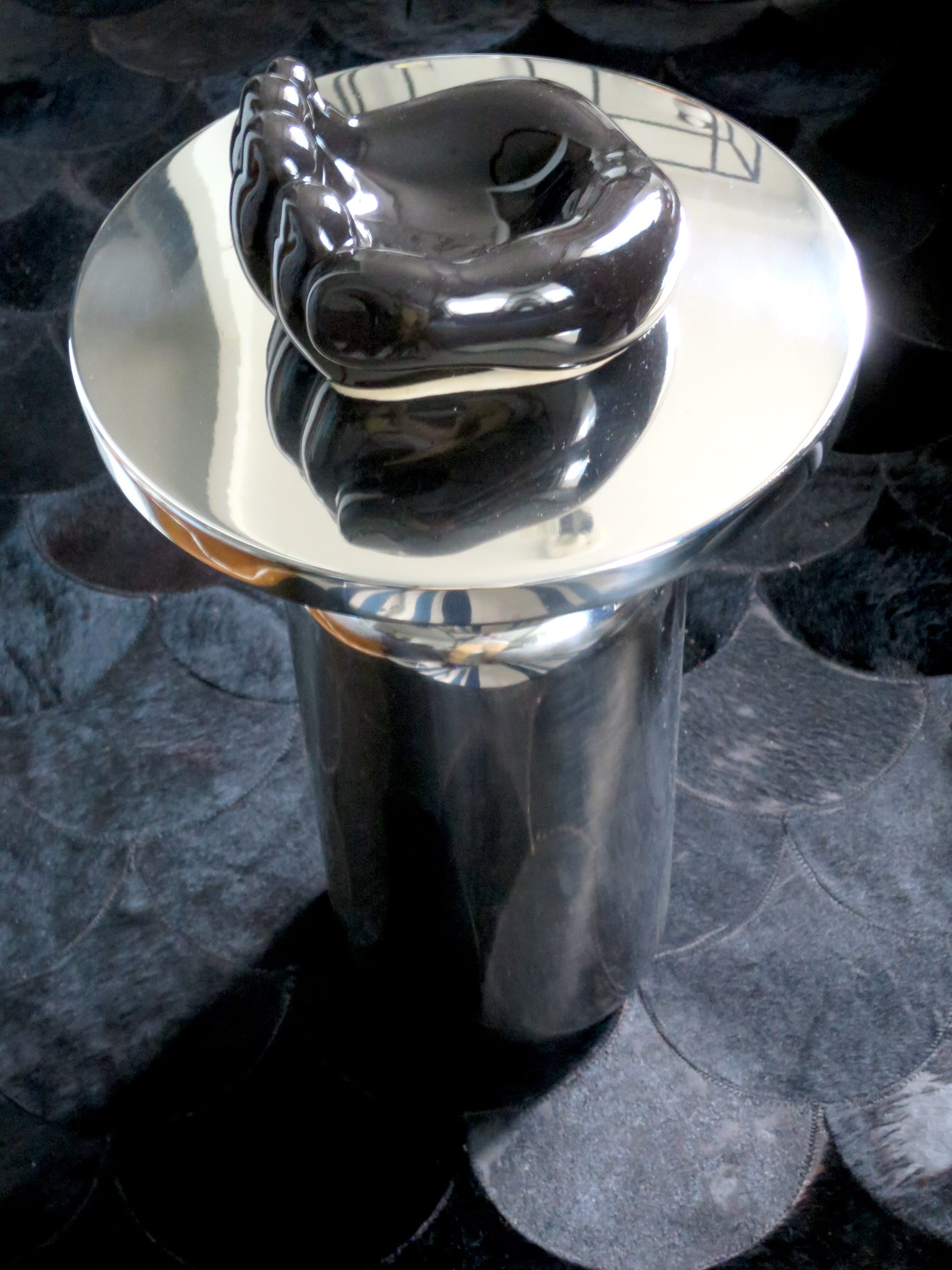 Black ceramic sculpture in the shape of a hand, resting on a side table made of polished aluminum.