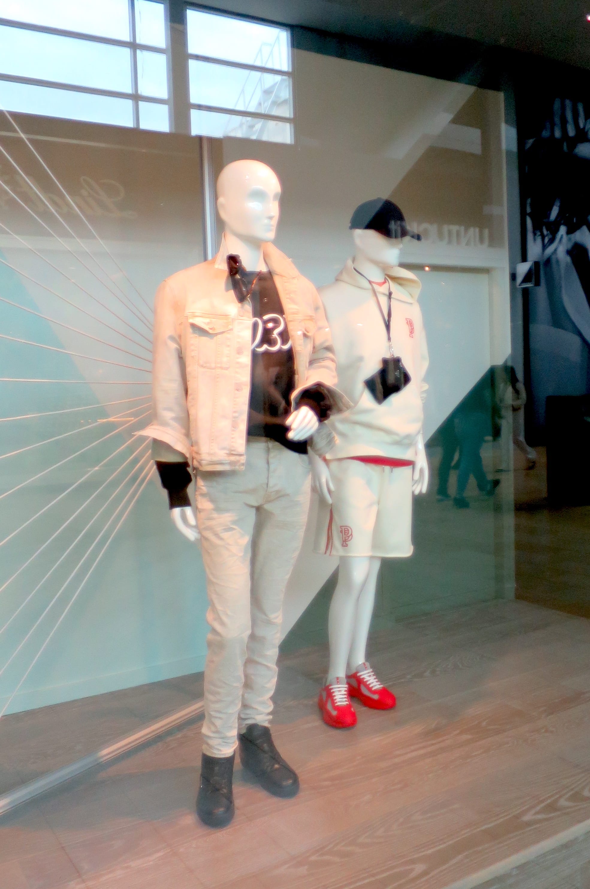 Two mannequins dressed in neutral tones, one with bright red sneakers.