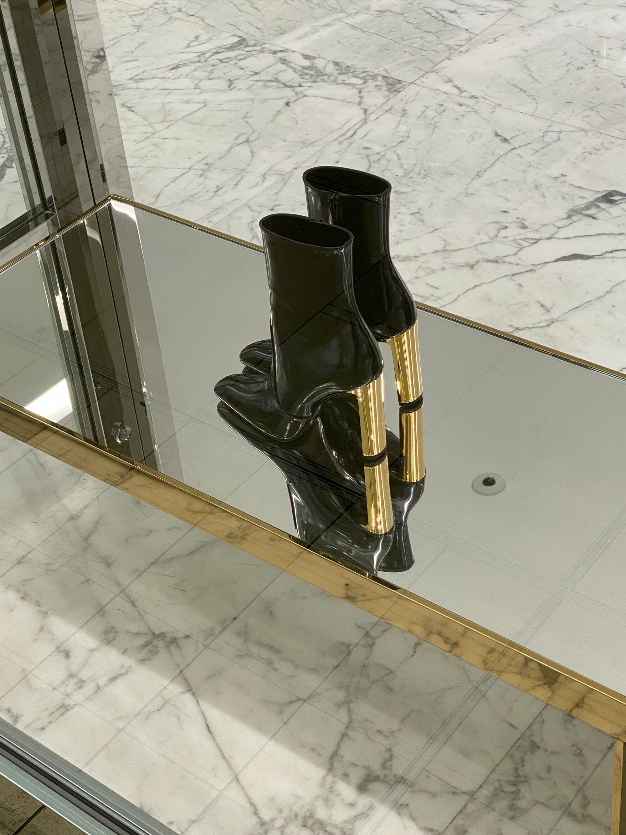 A pair of high-heeled boots displayed on a mirrored surface.