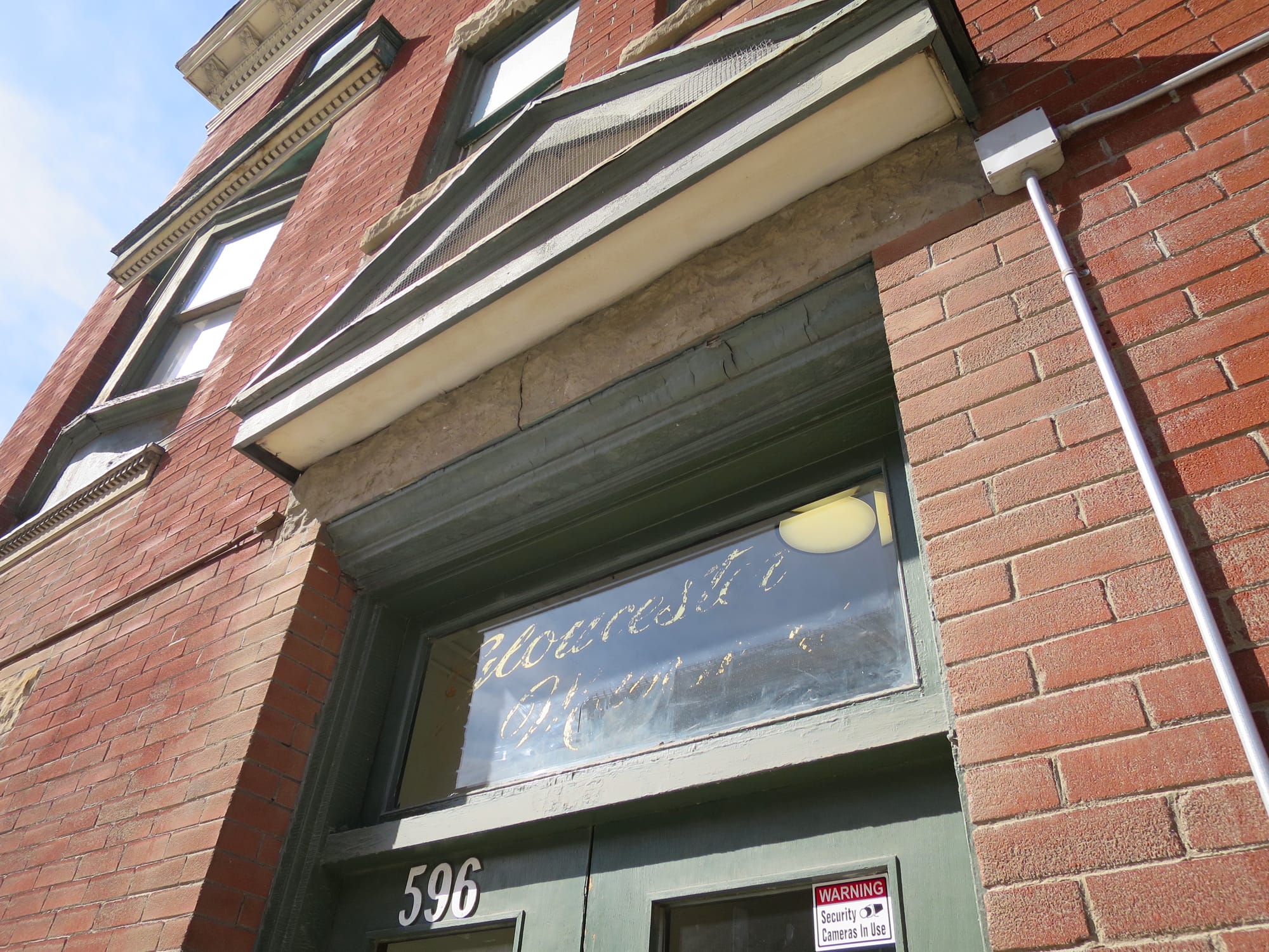 Entrance to a red brick building, with the words "Gloucester Mansions" painted on the window above the doors, the second word almost completely flaked away.