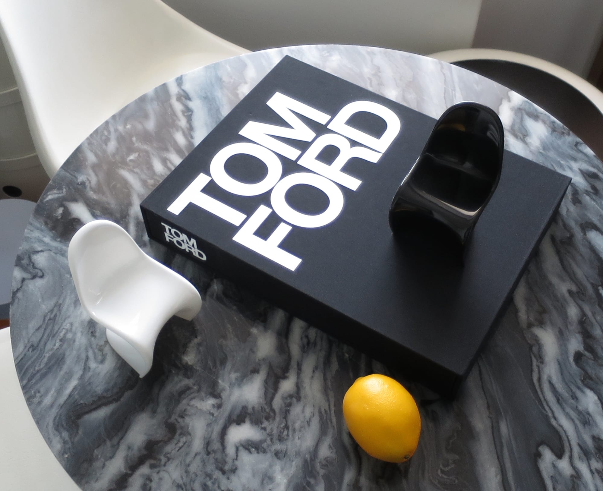 Tom Ford book on a marble dining table, along with two miniature chairs and a lemon.