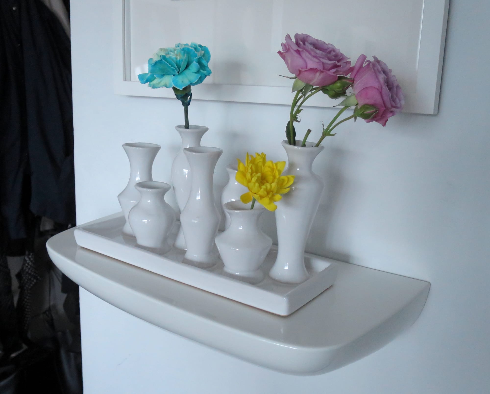 Seven white ceramic vases on a tray, with flowers displayed in three of them.