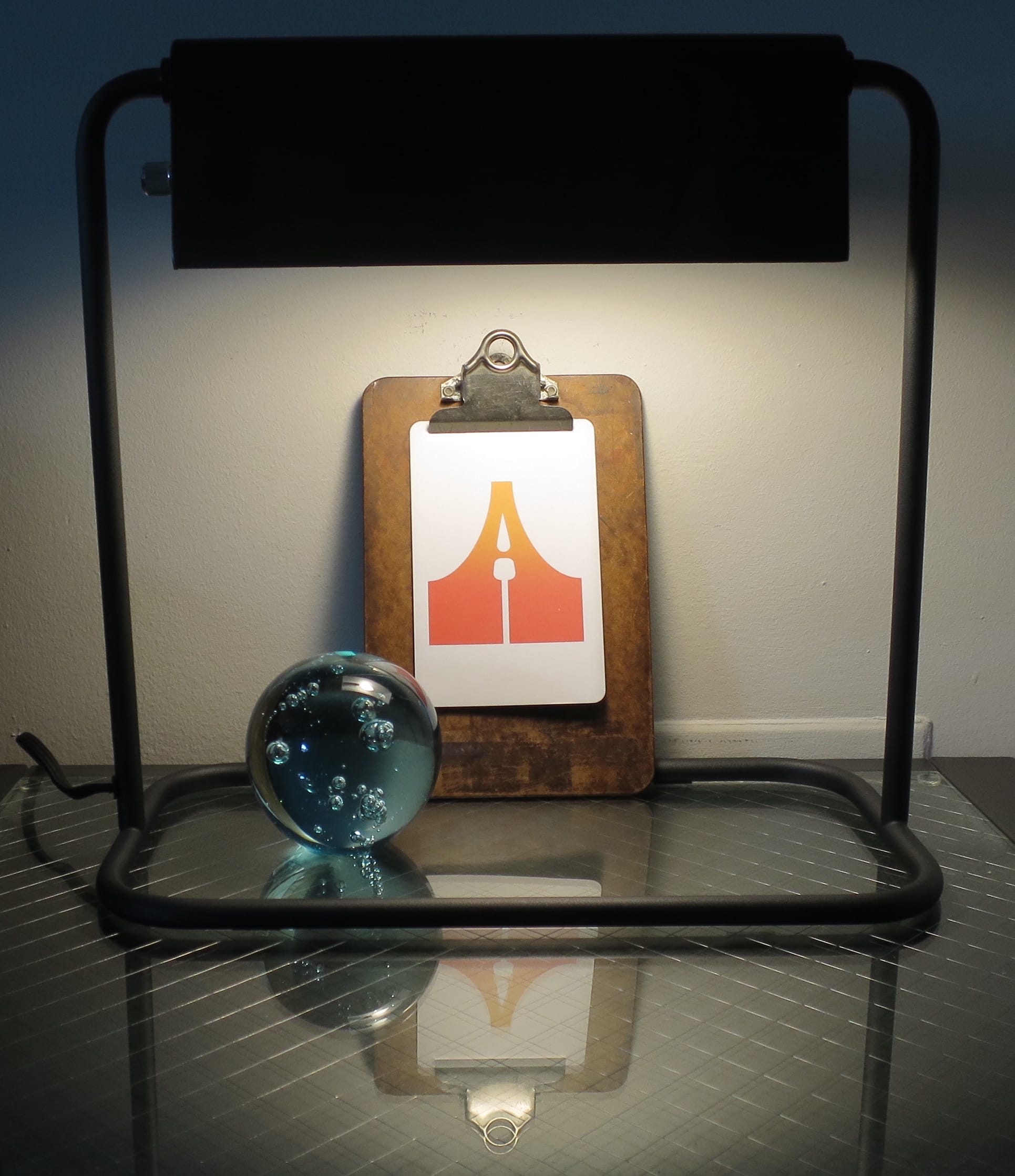 The same clipboard as above, framed by the base of a desk lamp.