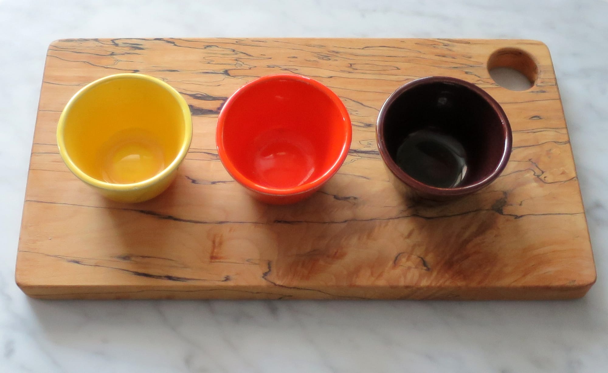 Three ceramic cups on a wooden cutting board.