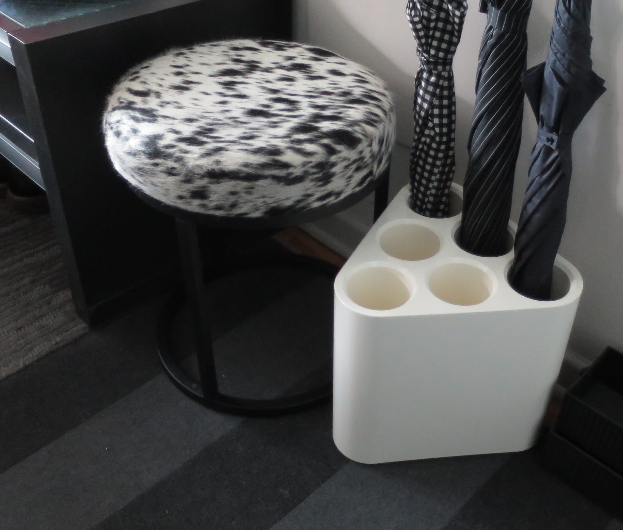 Black and white stool beside a white storage device holding three umbrellas.