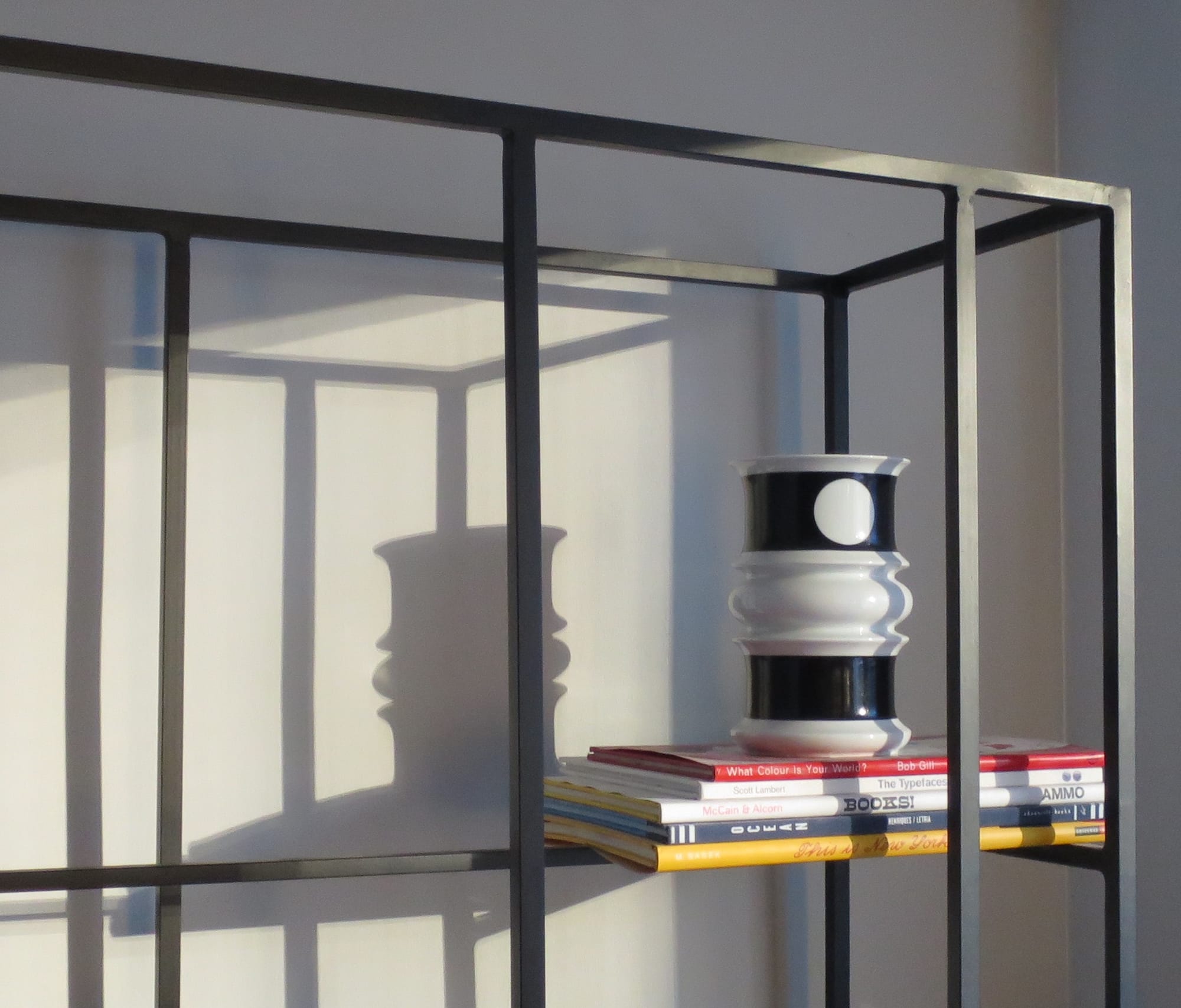 A modern black and white vase resting on a stack of books in a display unit.