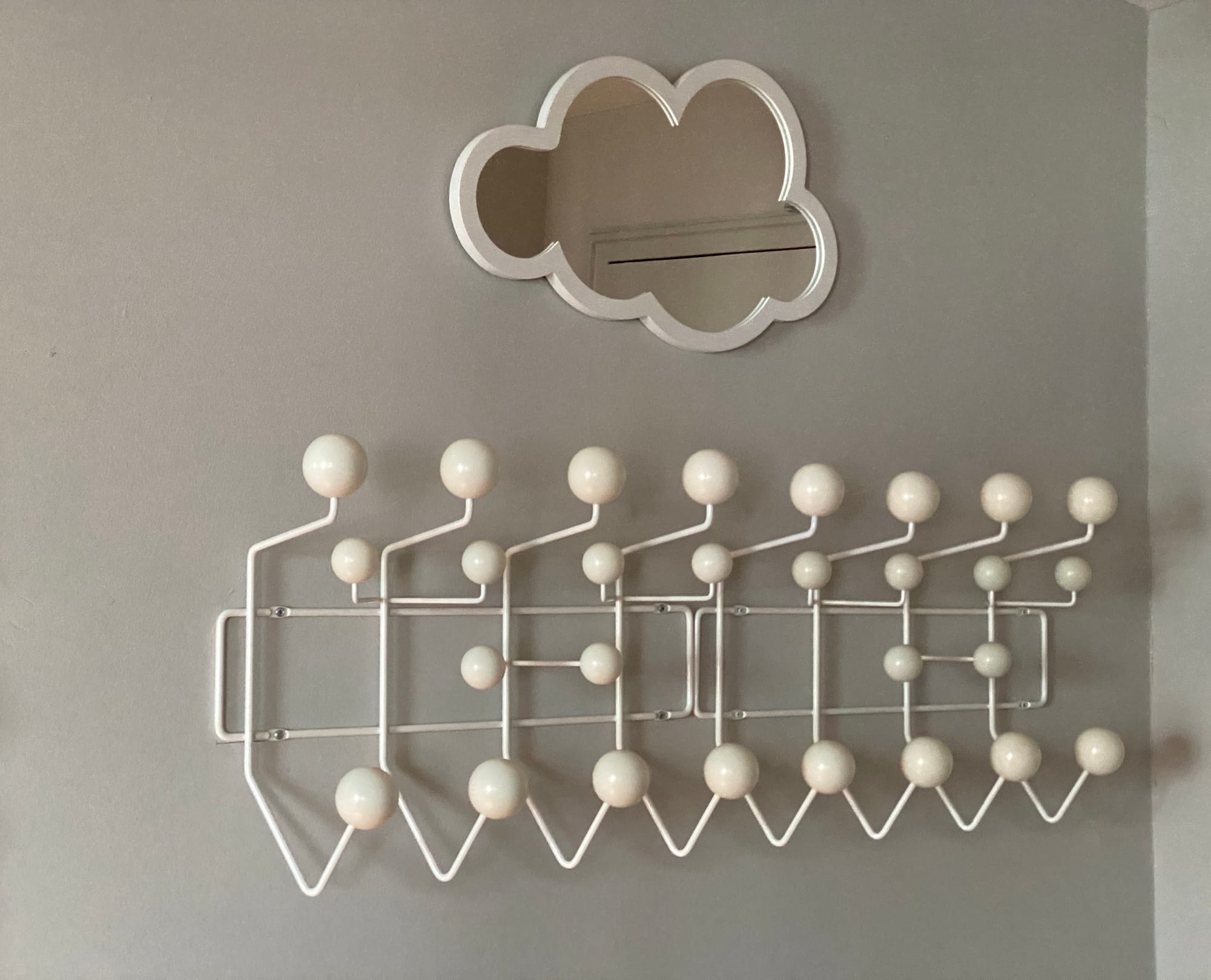 Mirror in the shape of a cloud, above two modular coat racks.