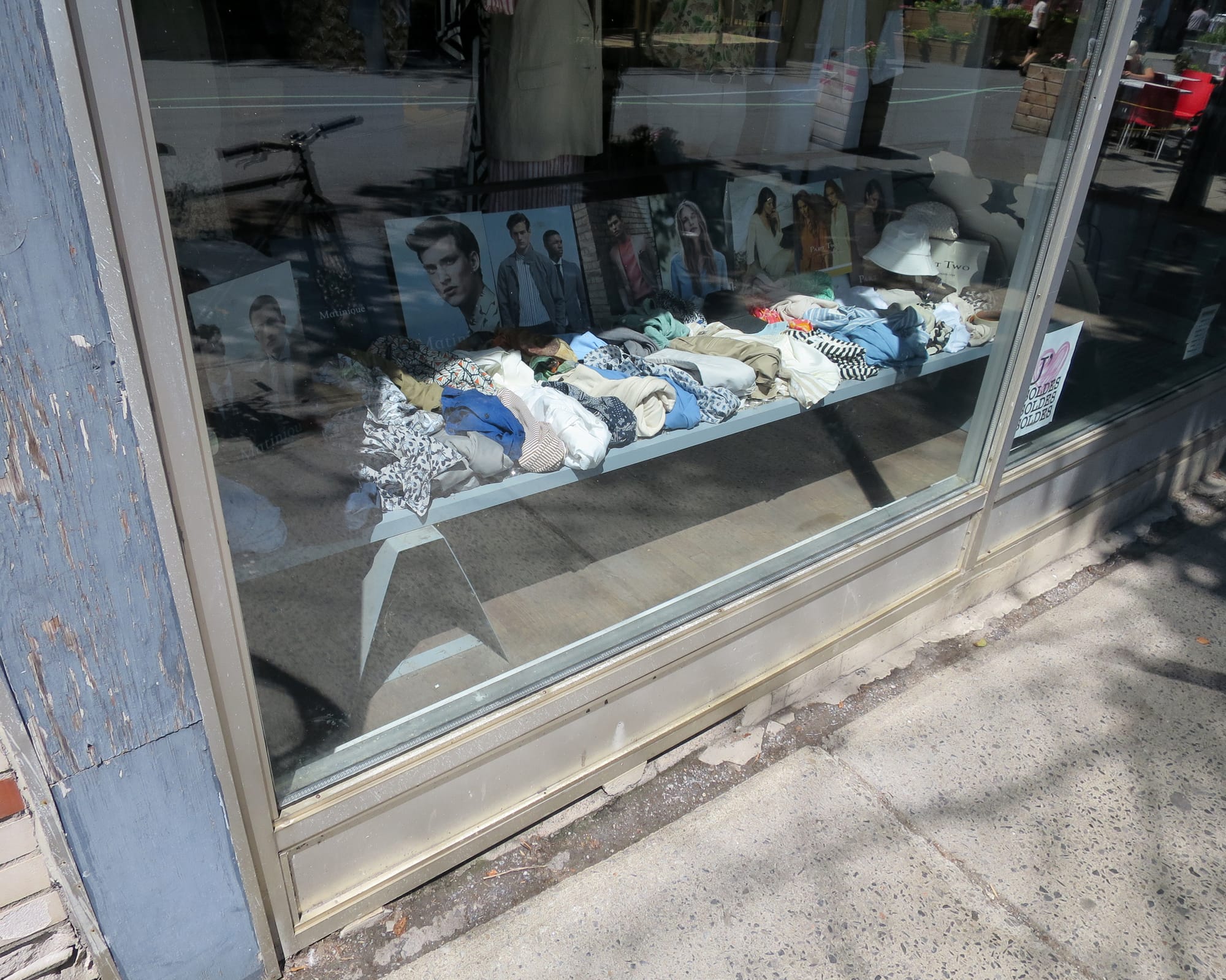 Shop window with a low table covered with crumpled items of clothing.