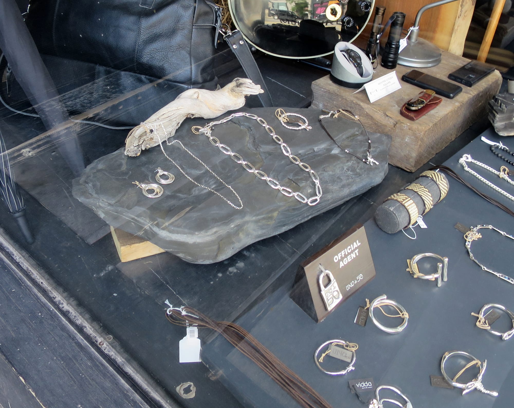 Shop window with a large rock and piece of driftwood as a backdrop for a jewelry display.