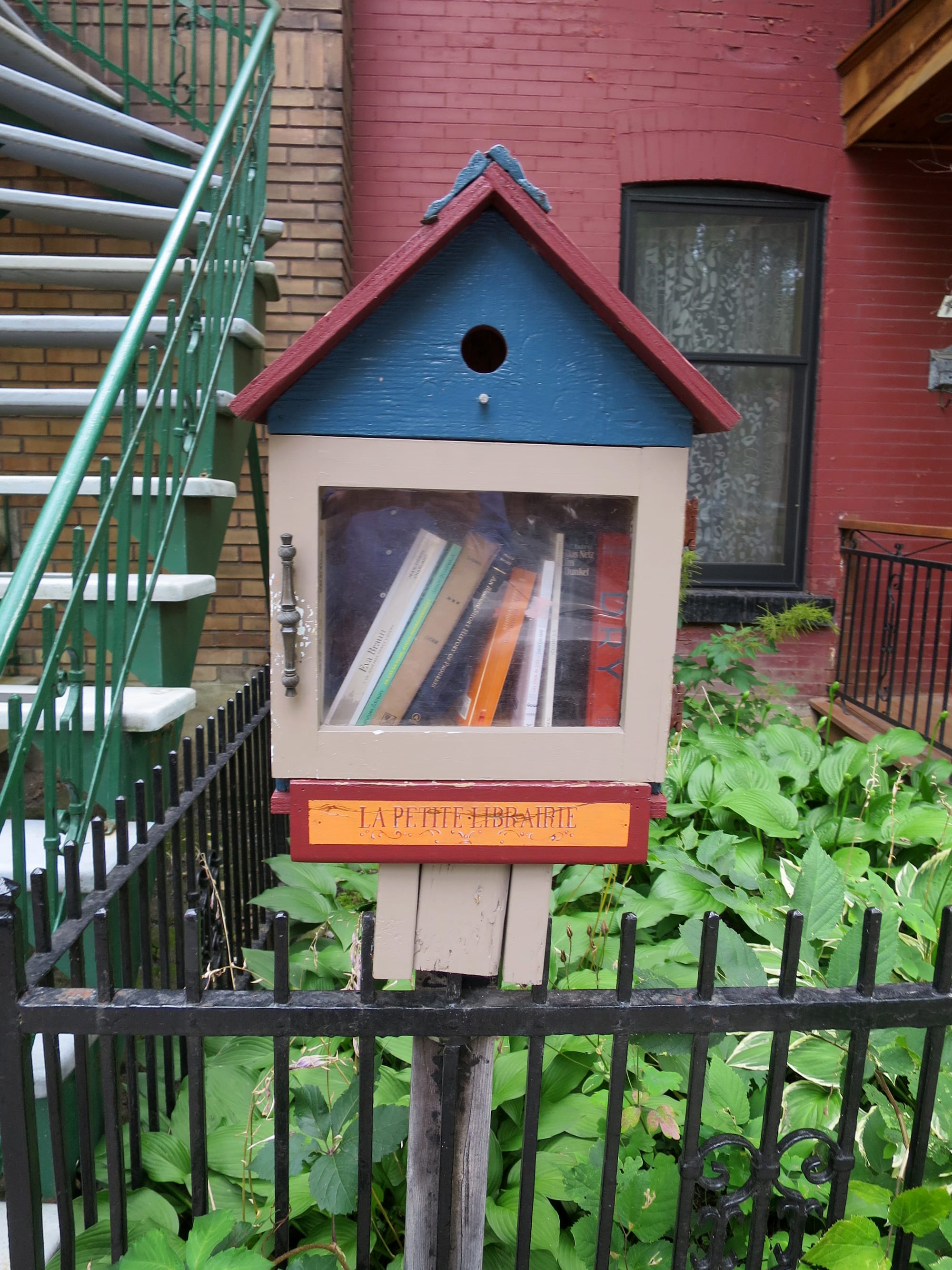 A little house on a pole, with books inside, and a sign reading "La Petite Librairie."