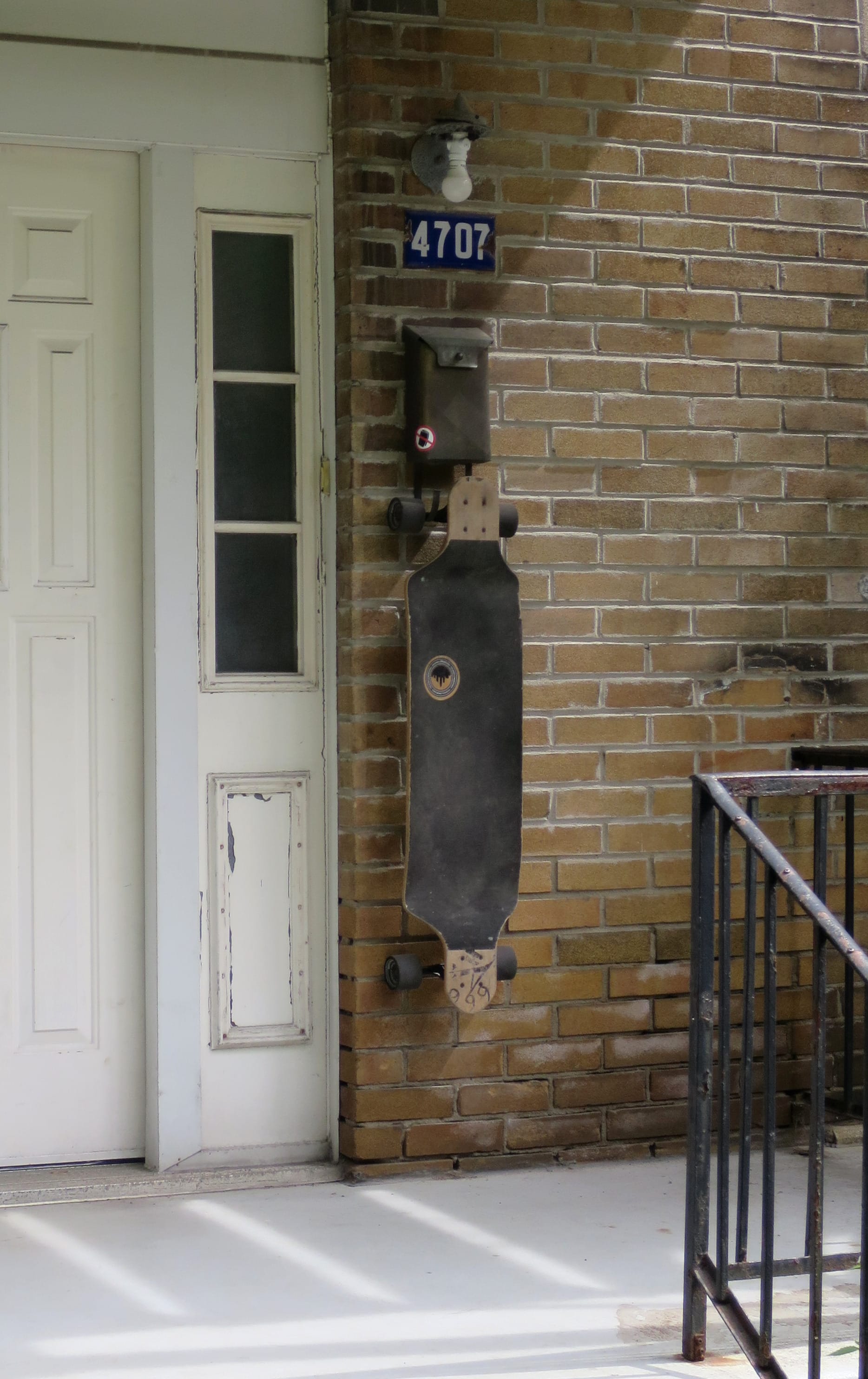 Skateboard hanging from hooks on a mailbox that were probably made for newspapers.