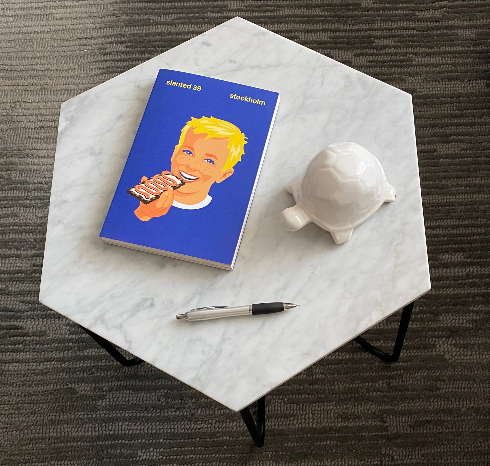 Small table inside Guy's apartment, featuring a Slanted magazine, a pen, and a turtle figurine.