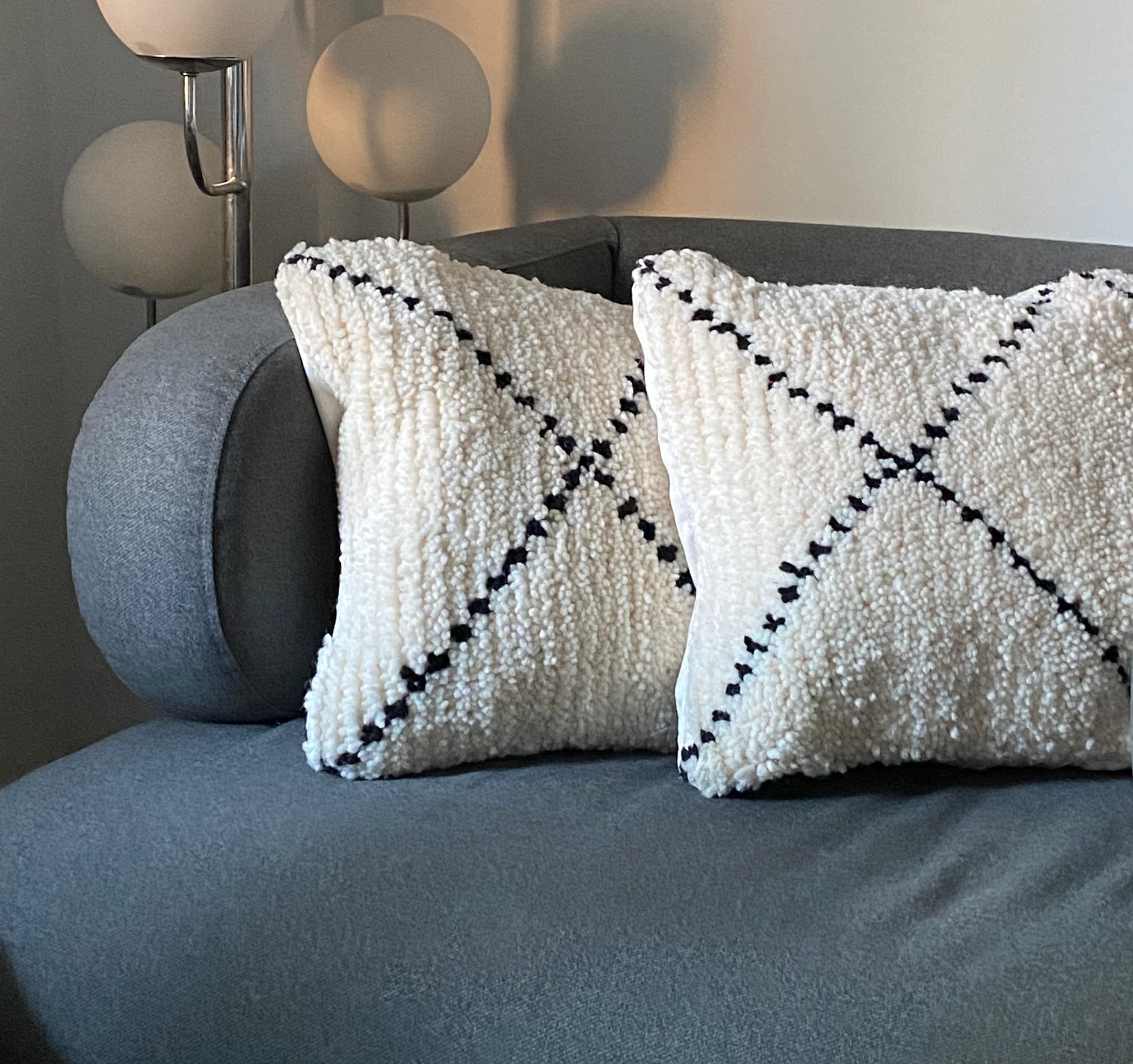 Two pillows, each with an X pattern, on a grey armchair.