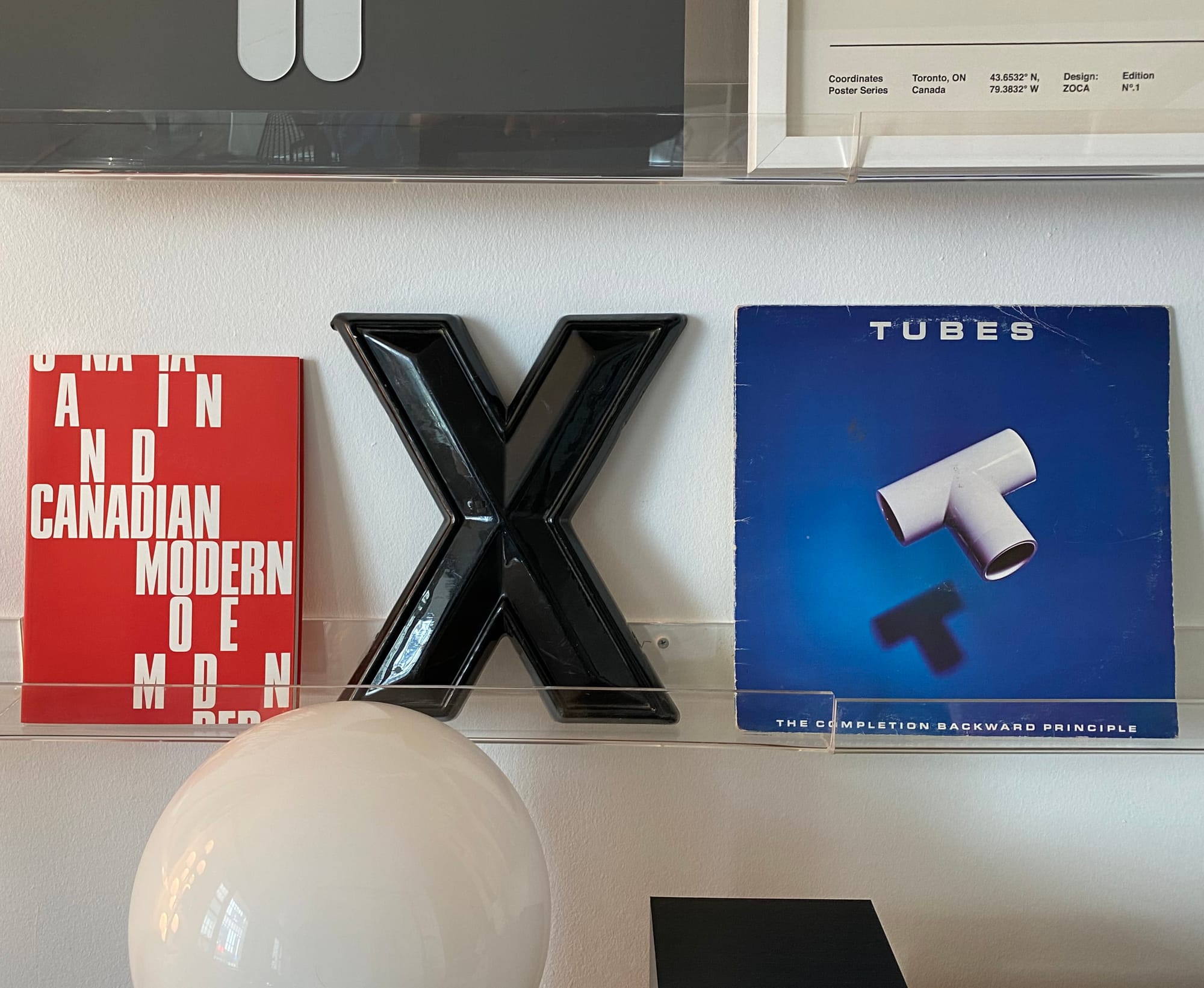 Acrylic wall shelf displaying an X from an old sign in between a book and an album cover.