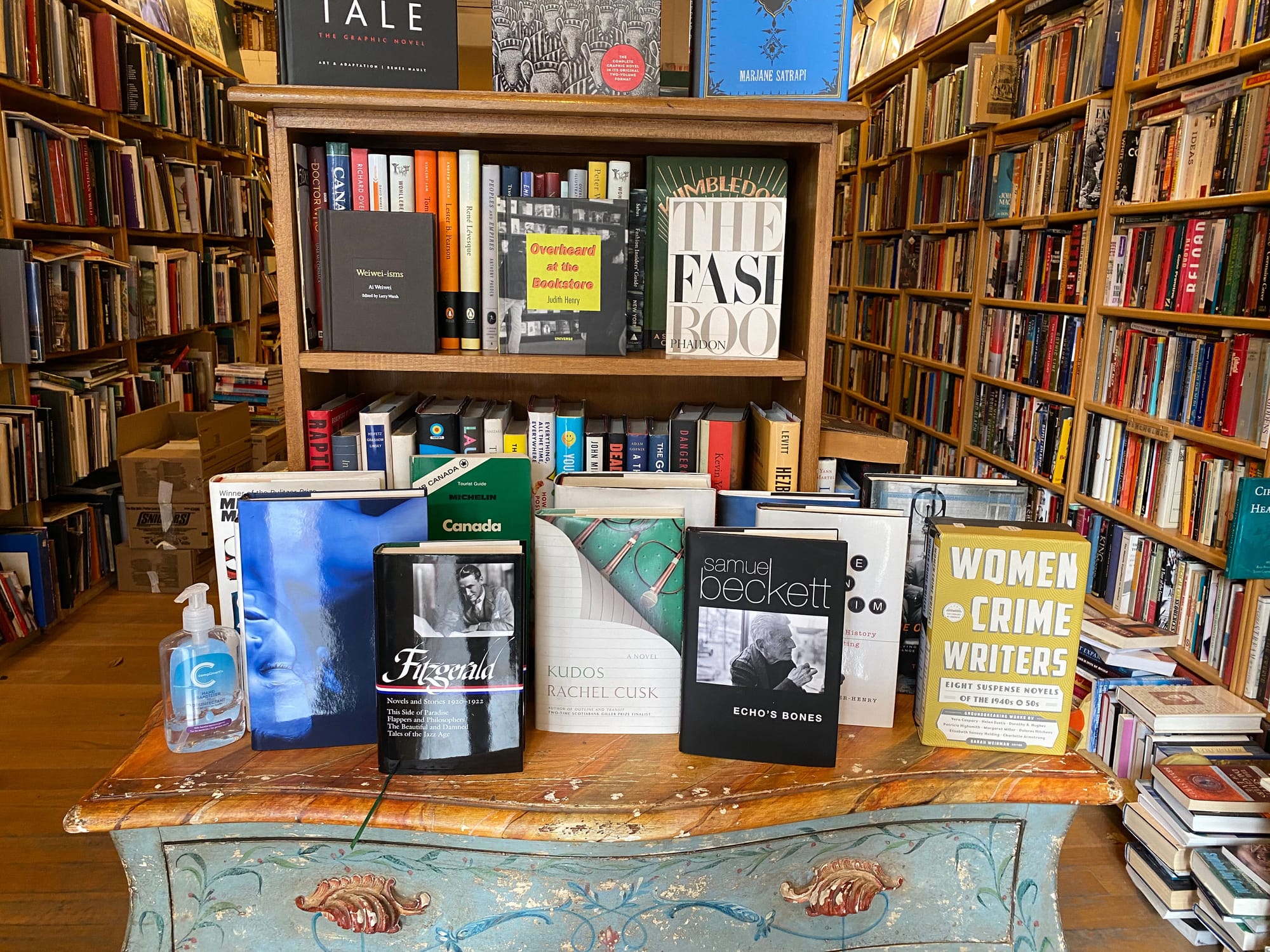 Interior of Balfour Books with a chest of drawers in the foreground, books standing upright on its surface.