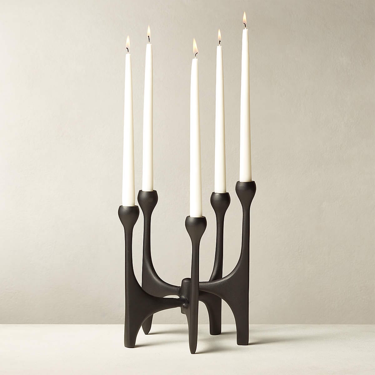 Smaller version of the same candelabra in black, holding five white candles that are lit.