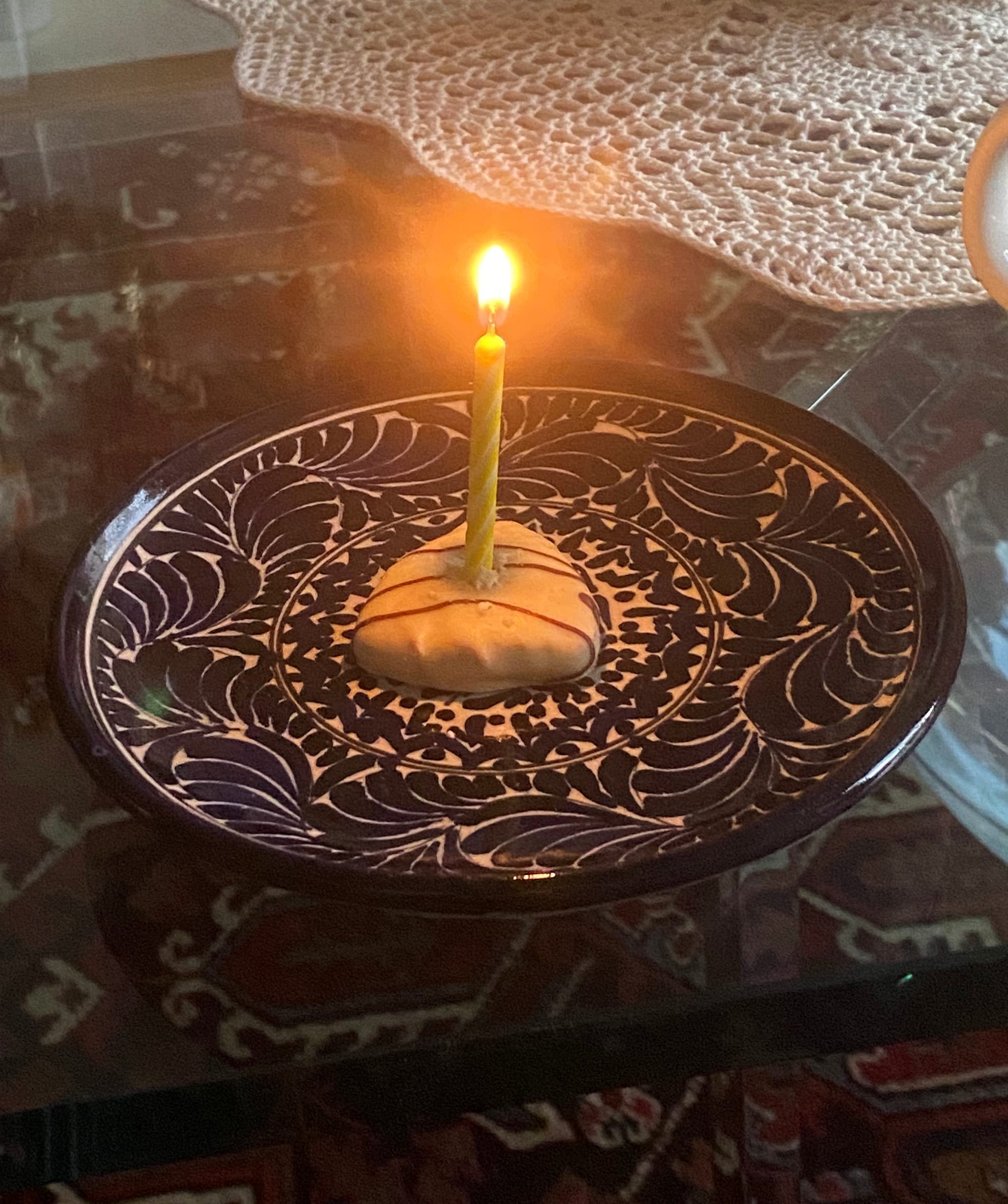 A yellow lit birthday candle planted in a small cookie that rests on a stylish saucer.