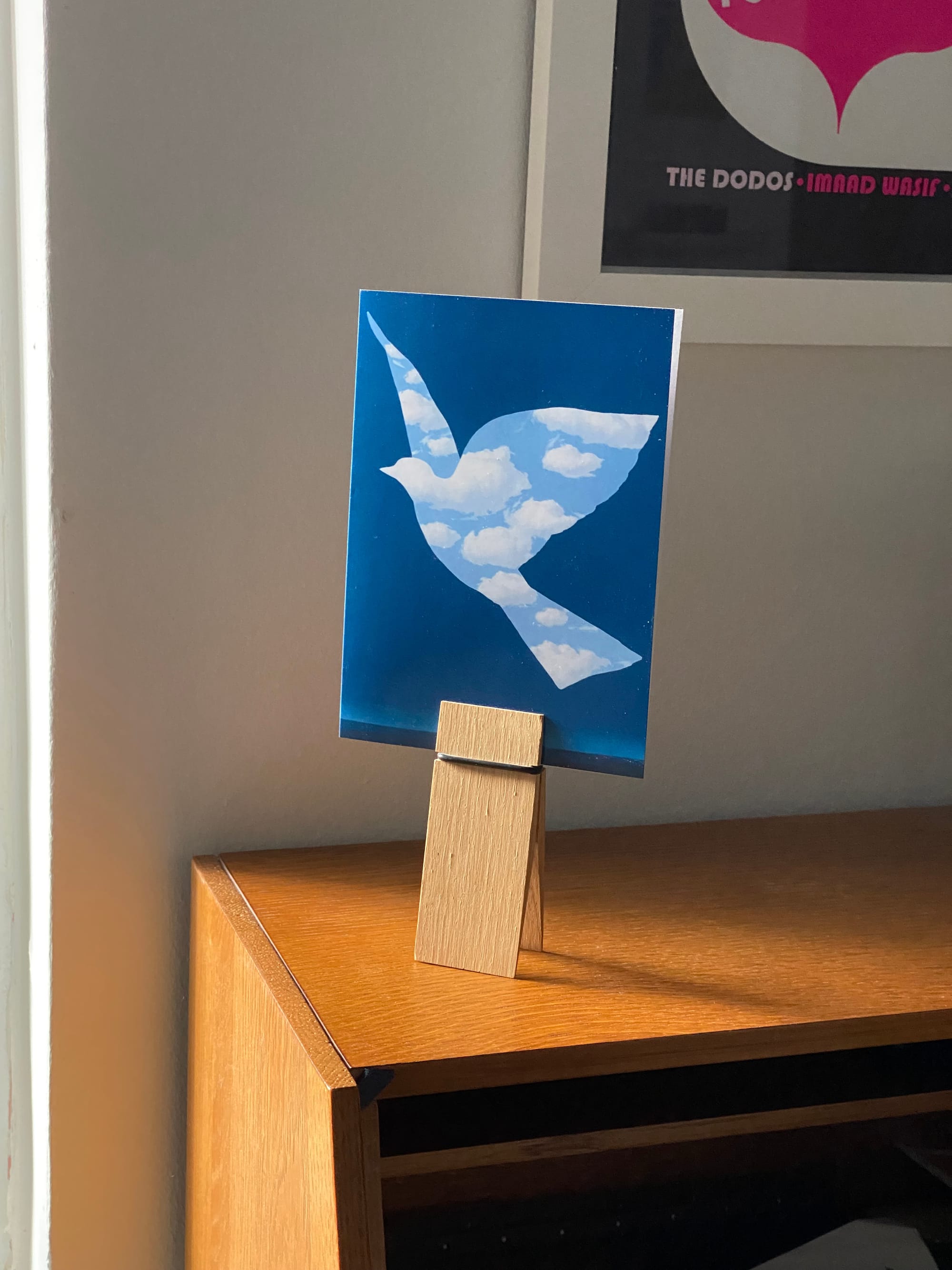 Card with a Magritte painting on the front, held up by a clothespin-like device on a desktop.