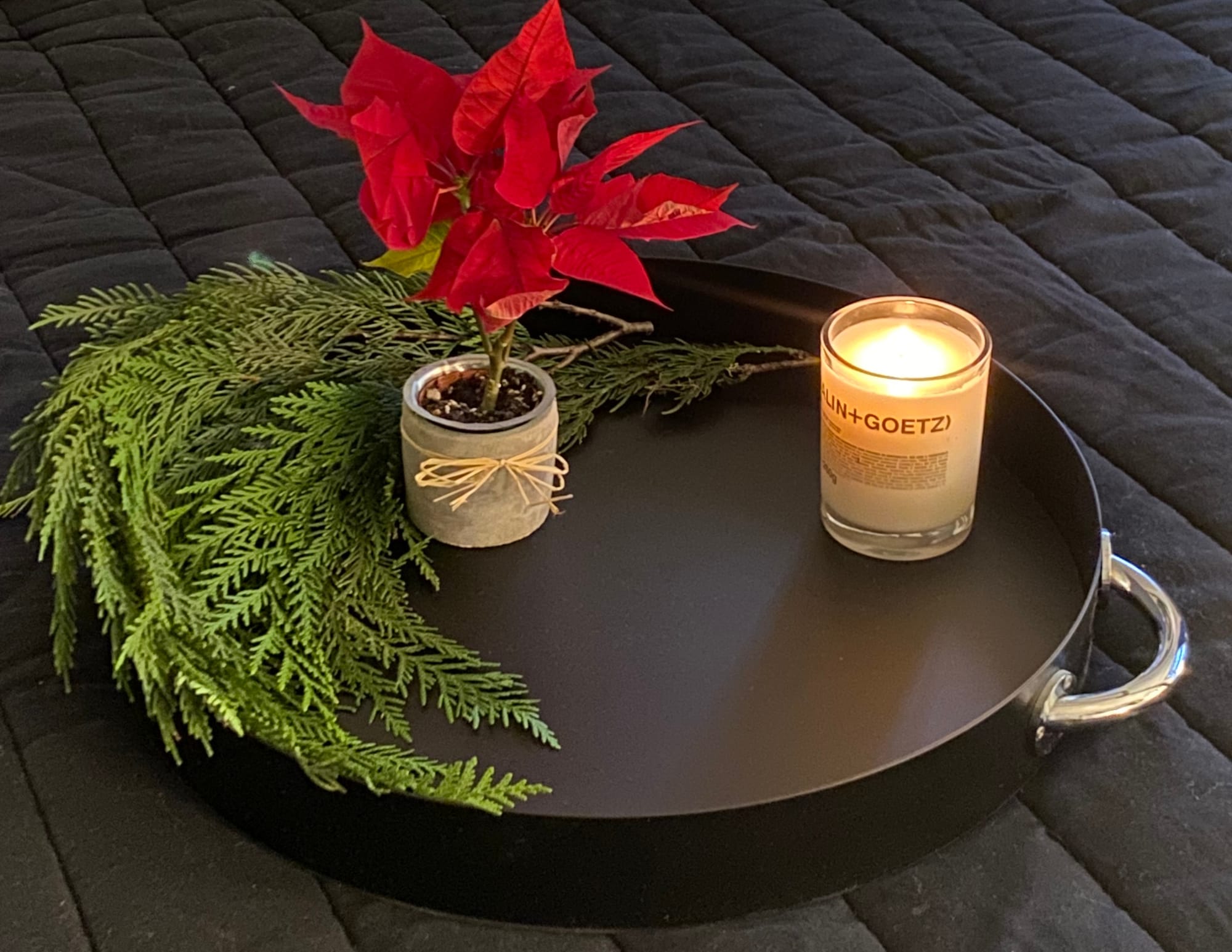 Tray resting on a black duvet, holding pine branches, a small poinsettia, and a candle.