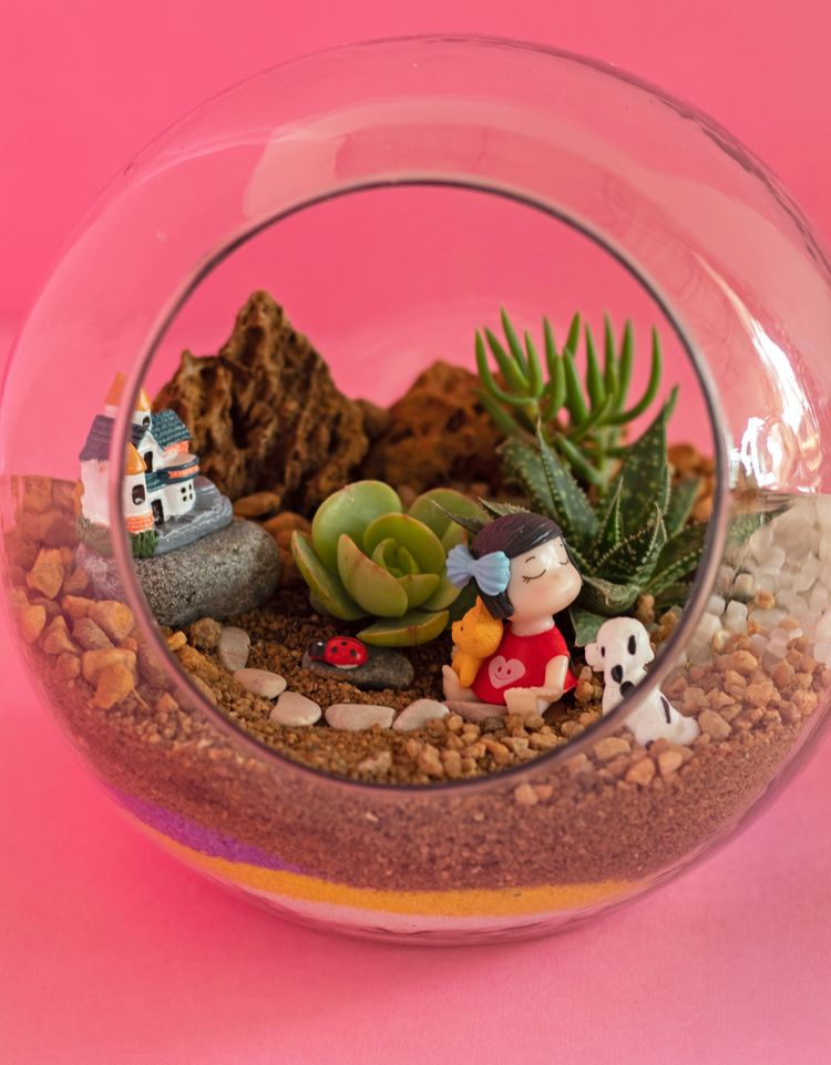 Succulents and figurines in a globe-shaped terrarium, including a little girl and a tiny house.