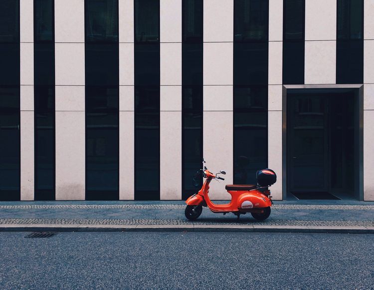 Motor scooter parked on a sidewalk in front of a wall with wide black-and-white stripes.