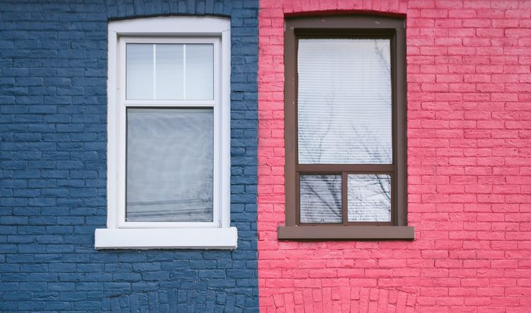 Windows of two adjoining townhouses, one with the facade painted dark blue, the other with the facade painted bright pink.