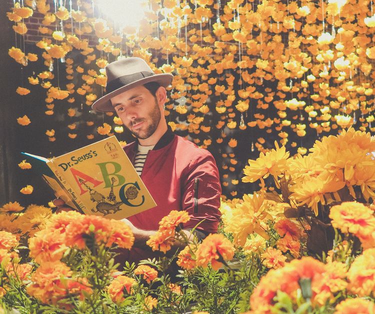 Stylish man reading Dr. Seuss's ABC while surrounded by orange flowers.