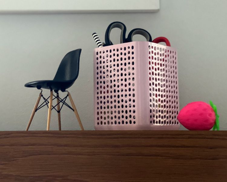 Miniature chair, container of office supplies, and plastic strawberry on a desktop.