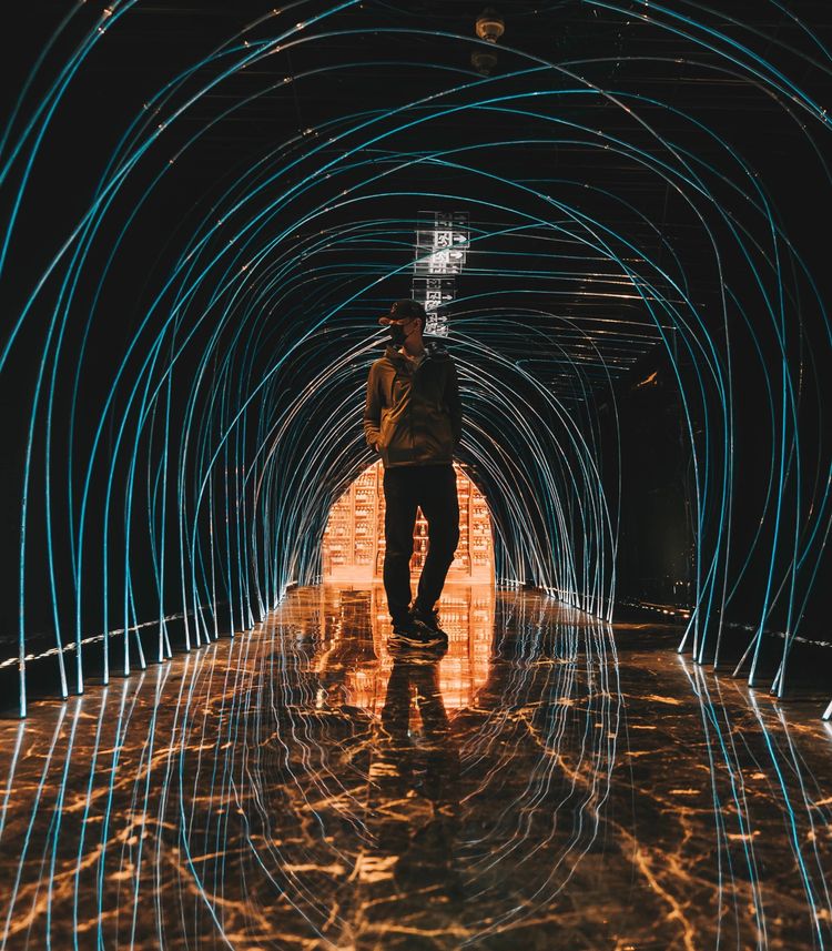 Young man in dark clothing walking on a sleek marble floor in a dimly lit tunnel.