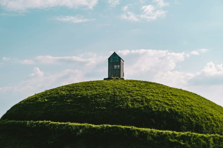 Small wooden structure all alone at the top of a grassy hill.