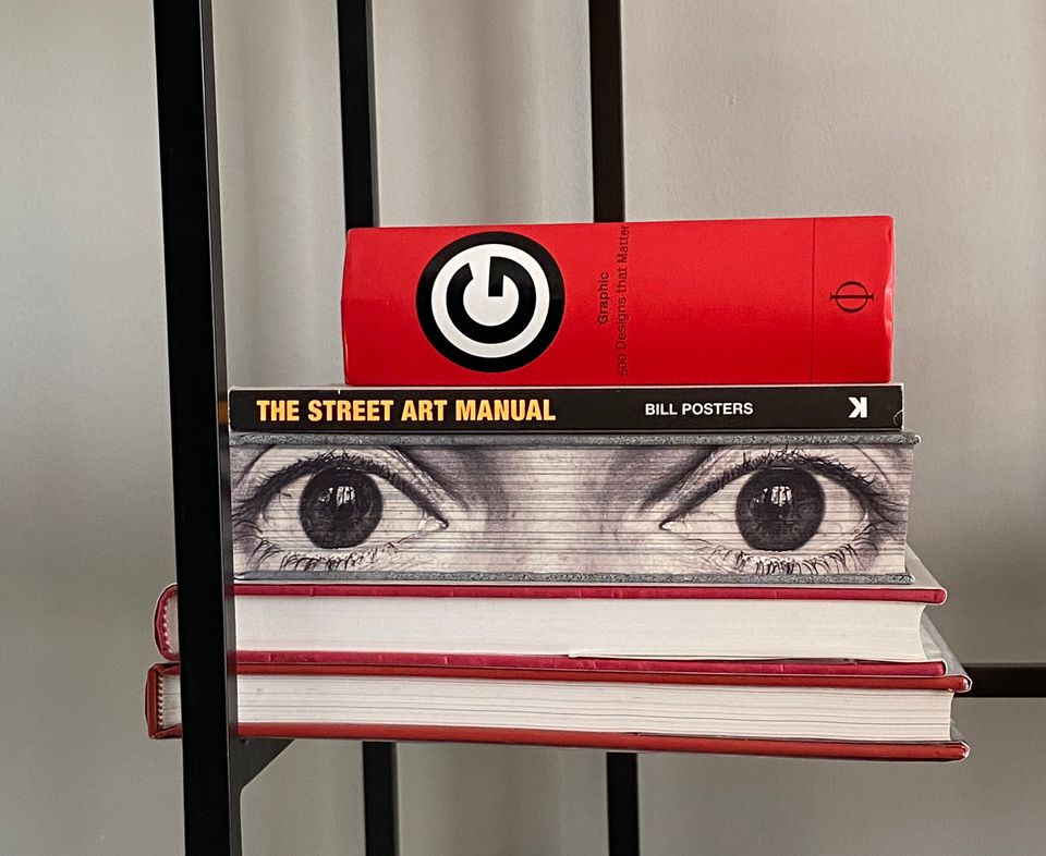 Stack of five books, including one with a close-up of wide-open eyes printed on the sheaf of pages.