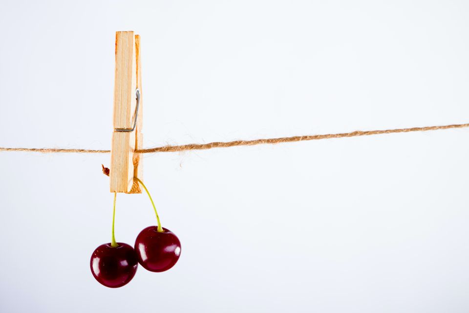 Pair of cherries suspended from a string by a clothespin.